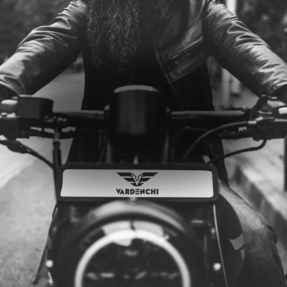Vardenchi 桌布 壁紙 — 一位留鬍子的騎手穿著皮夾克，在充滿氣氛的黑白街頭照片中握著VARDENCHI電單車的把手。