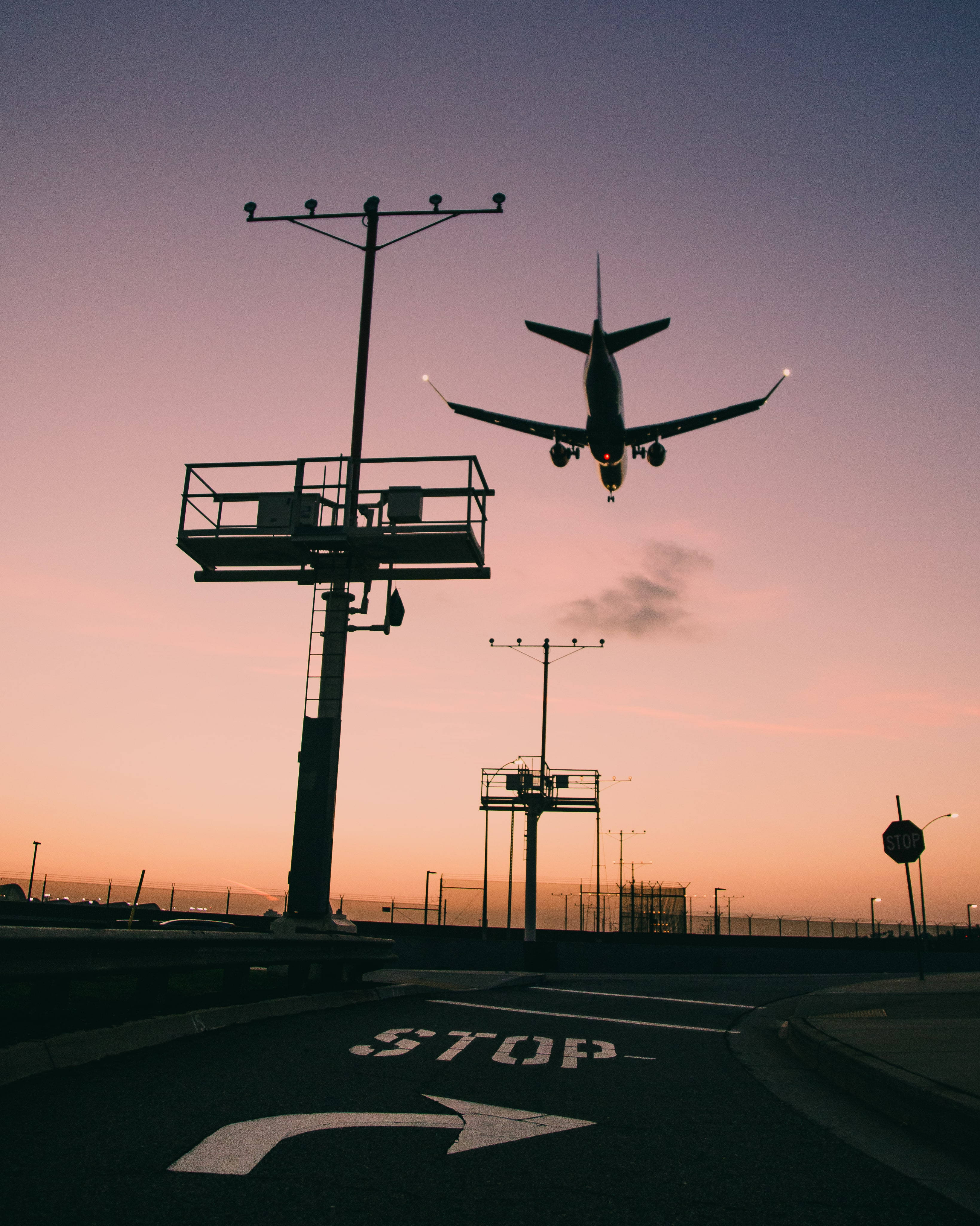 下一站：LAX 壁紙 — 一架商用客機在鮮豔的粉紅色和橙色日落襯托下，呈現剪影，正下降至機場跑道。