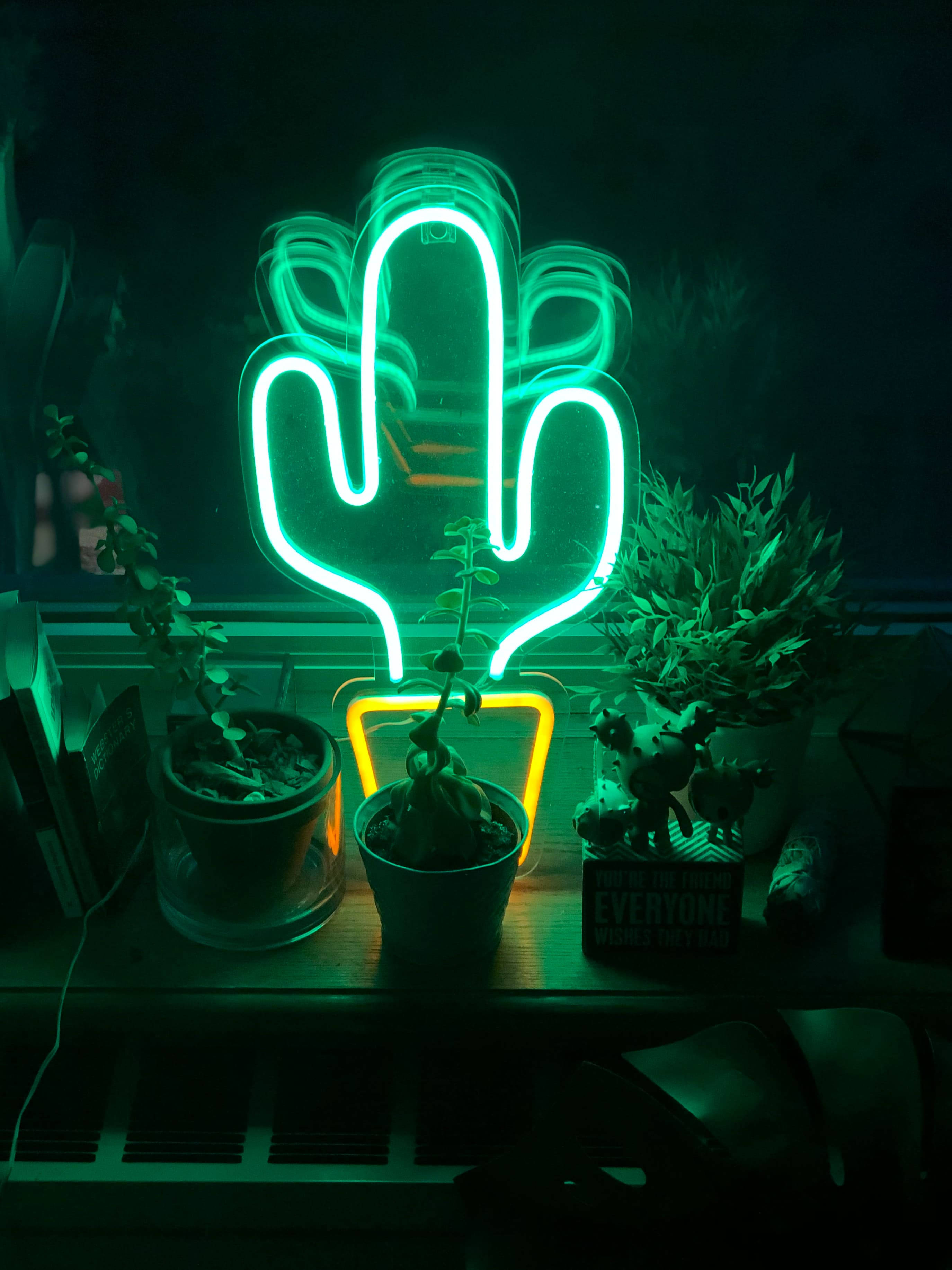 LED霓虹綠仙人掌 壁紙 — 發光的綠色霓虹仙人掌燈在深色木架上投射出詭異的光芒，照亮盆栽植物和小雕像。