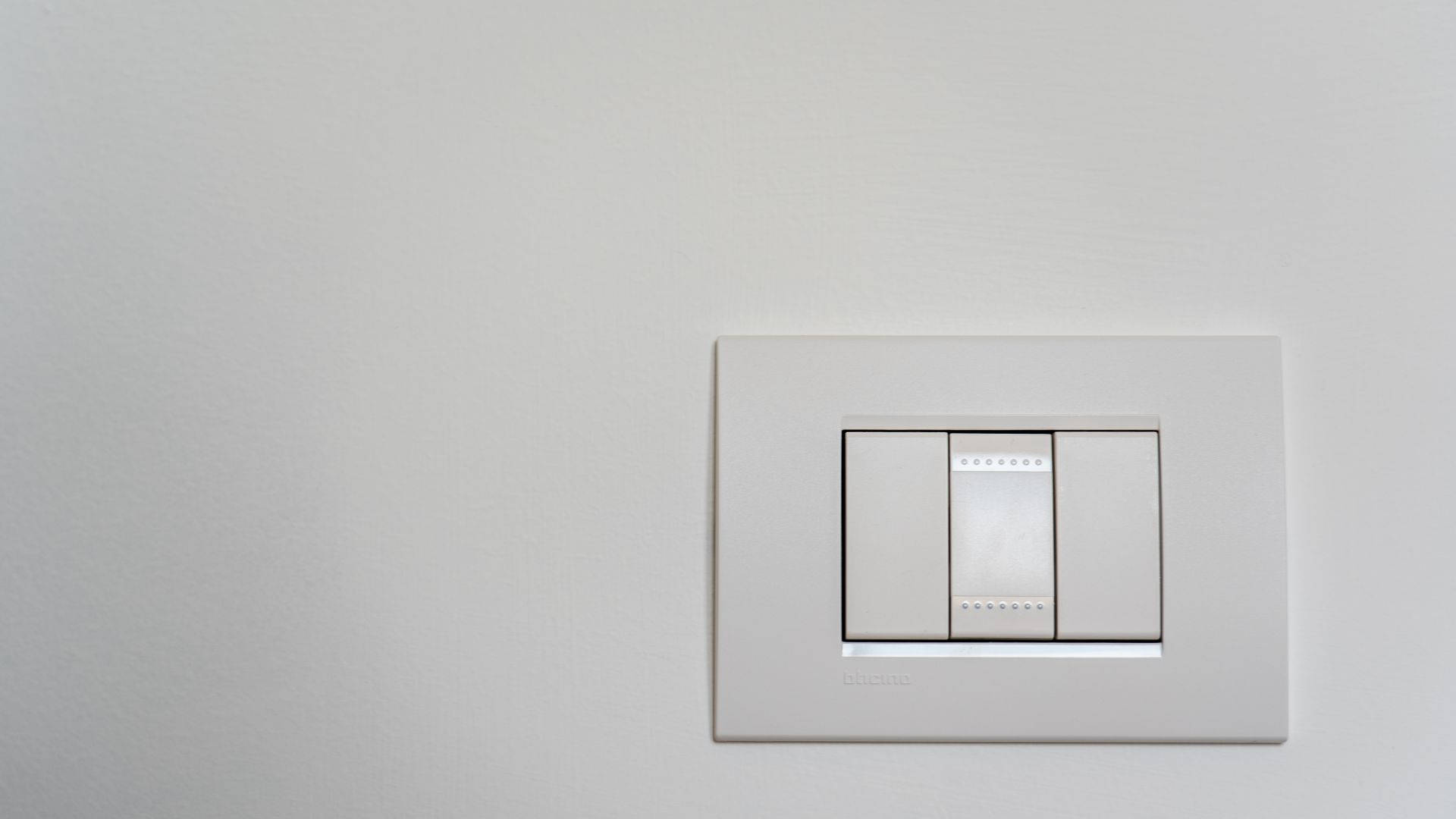 Legrand 智慧電燈開關 壁紙 — 一個極簡風格的白色燈掣面板，帶有三個撥動開關，安裝在純色米白色牆上。