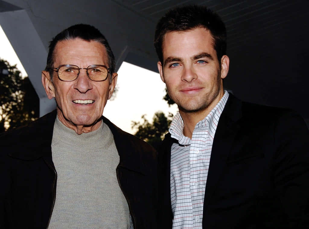 美國演員 Leonard Nimoy 與 Chris Pine 壁紙 — 兩名男子，一位戴眼鏡較年長，另一位藍眼睛較年輕，在現代建築結構下並肩微笑站立。