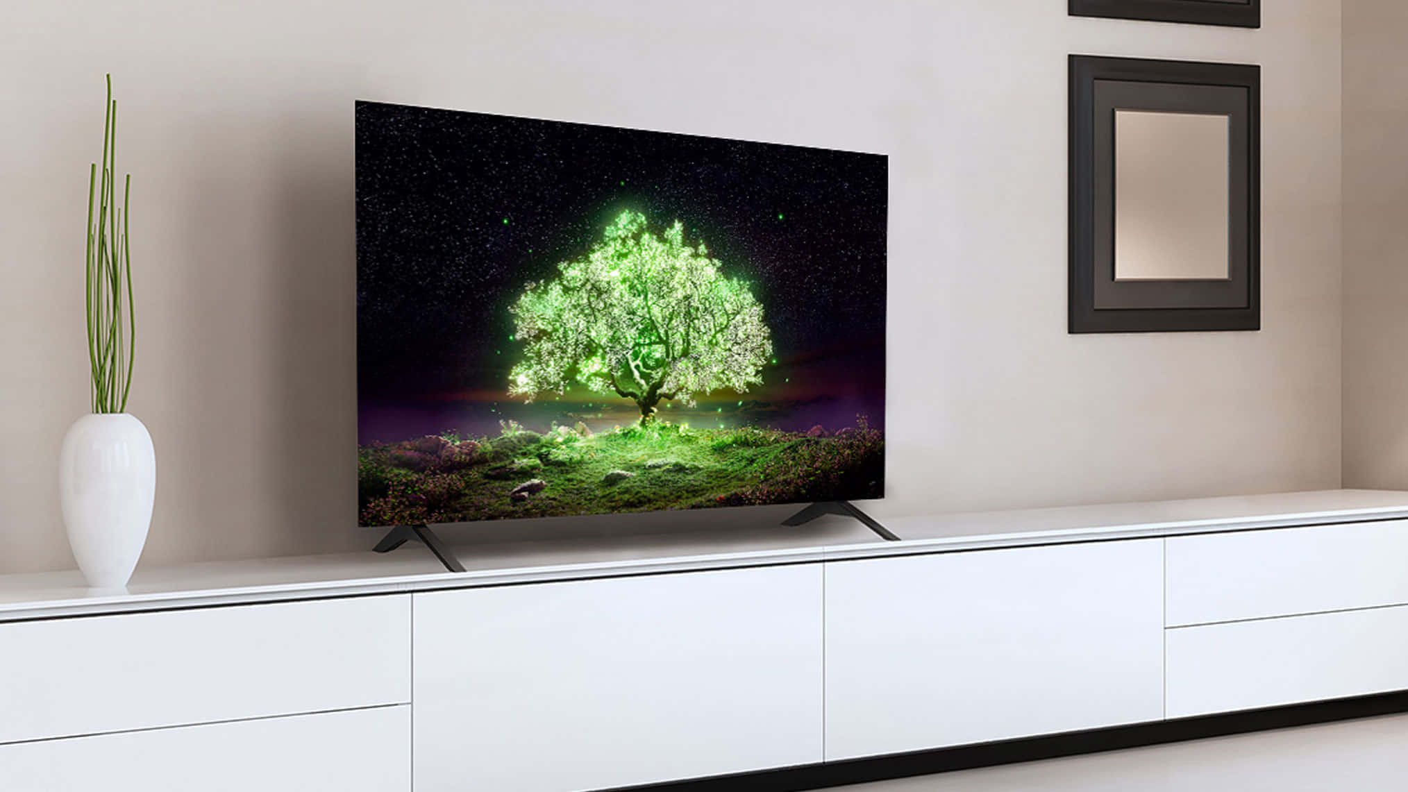 LG OLED A1電視畫面 壁紙 — 一部時尚電視顯示一棵在星空下發光的綠色樹木，置於簡約白色娛樂櫃上。