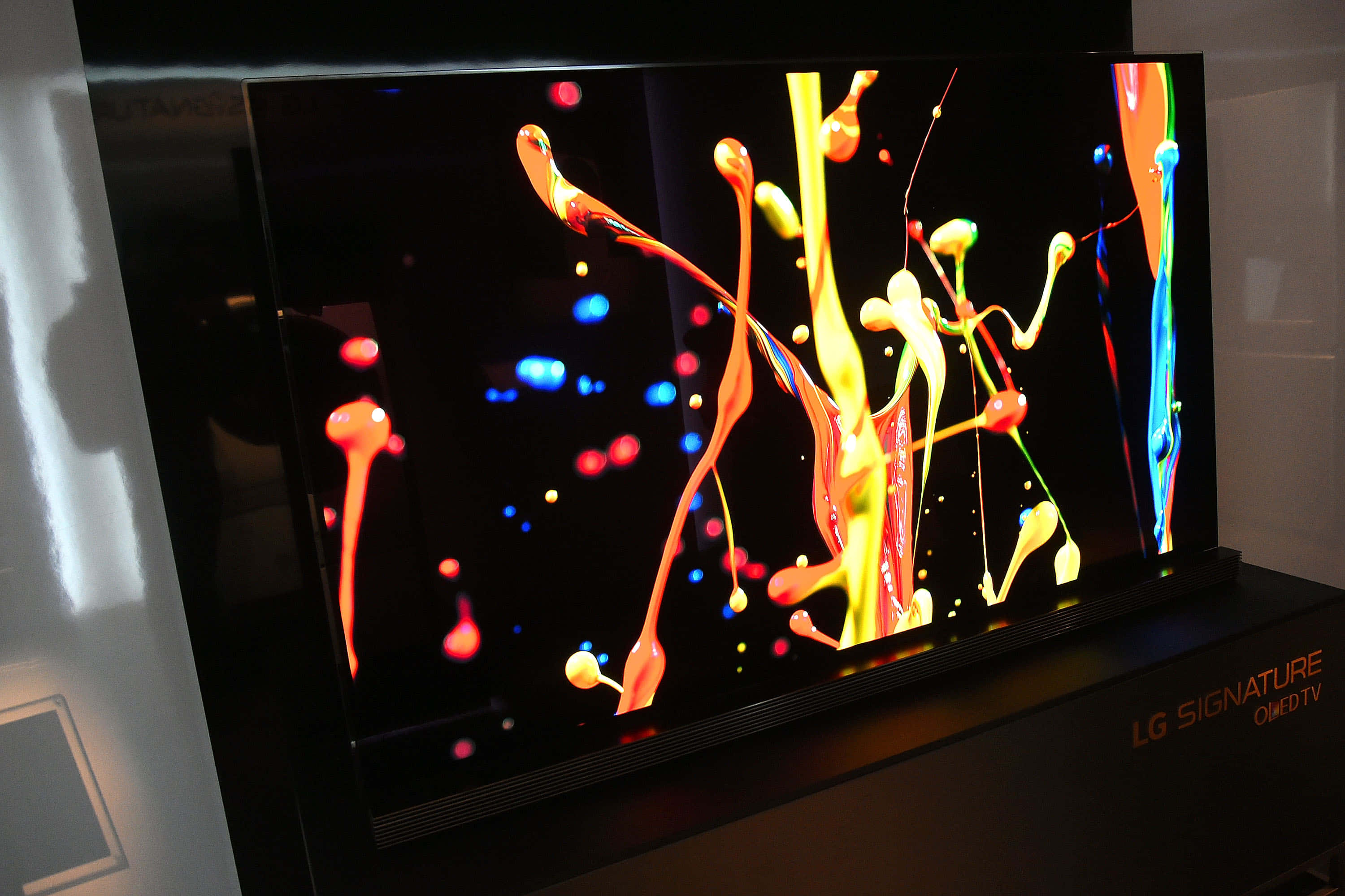 LG Signature OLED電視畫面 壁紙 — 一部時尚的LG Signature OLED電視在黑色背景上顯示出充滿活力的抽象彩色油漆飛濺。