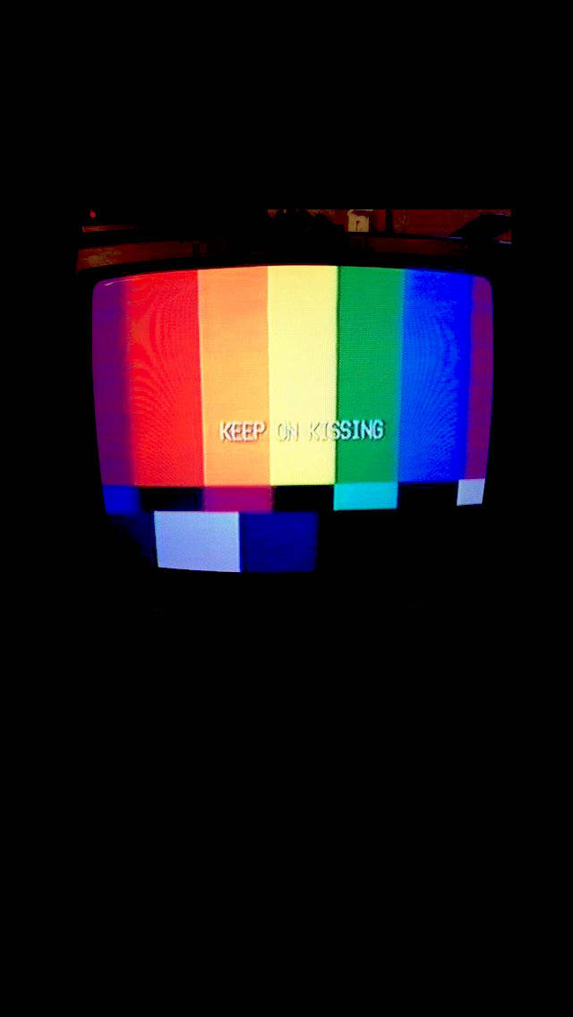 以鮮豔色彩慶祝LGBT+驕傲 壁紙 — 一部復古CRT電視顯示彩色測試圖案，文字「keep on kissing」在黑暗環境中發出白色光芒。