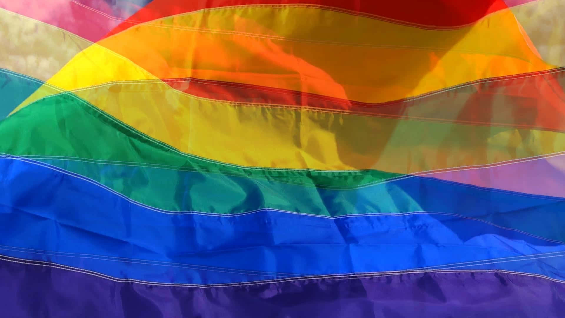 以 LGBT 旗幟慶祝自豪 壁紙 — 一面鮮豔的彩虹旗在風中飄揚，帶有紅、橙、黃、綠、藍、紫的鮮明條紋。