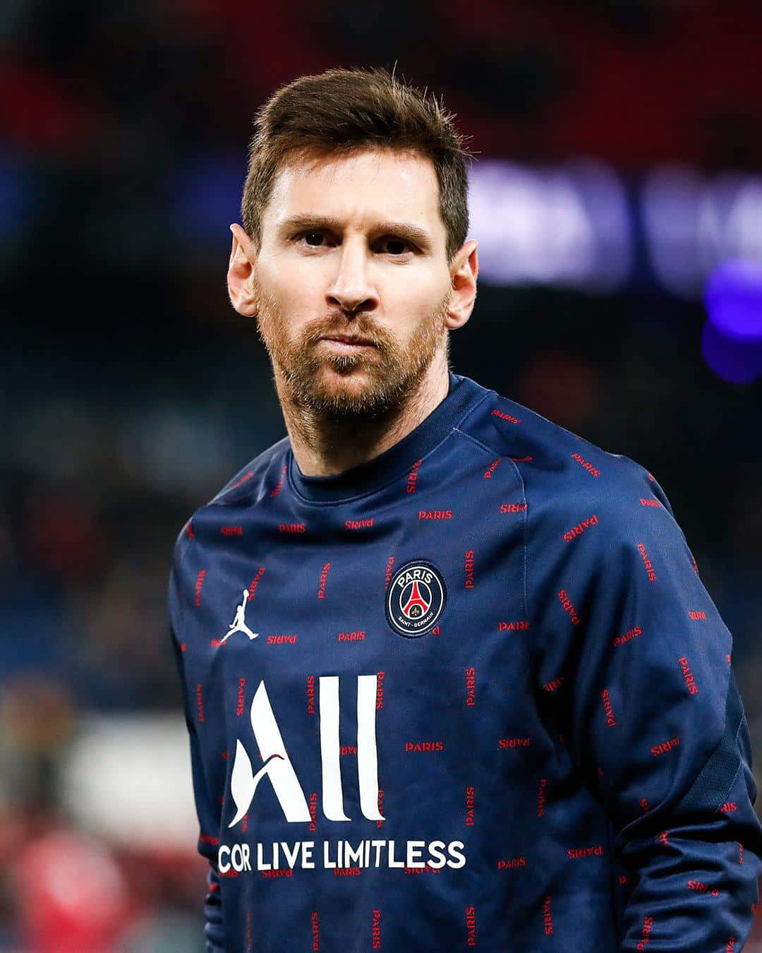 Messi 2022 桌布 壁紙 — 利安奴·美斯身穿巴黎聖日耳曼訓練上衣，在球場燈光下專注地凝視鏡頭。
