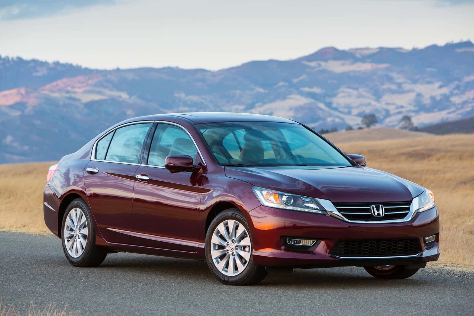 Honda Accord 桌布 壁紙 — 一輛栗色本田雅閣轎車在鋪砌的道路上閃閃發光，背景是起伏的丘陵和遠山，天空柔和。