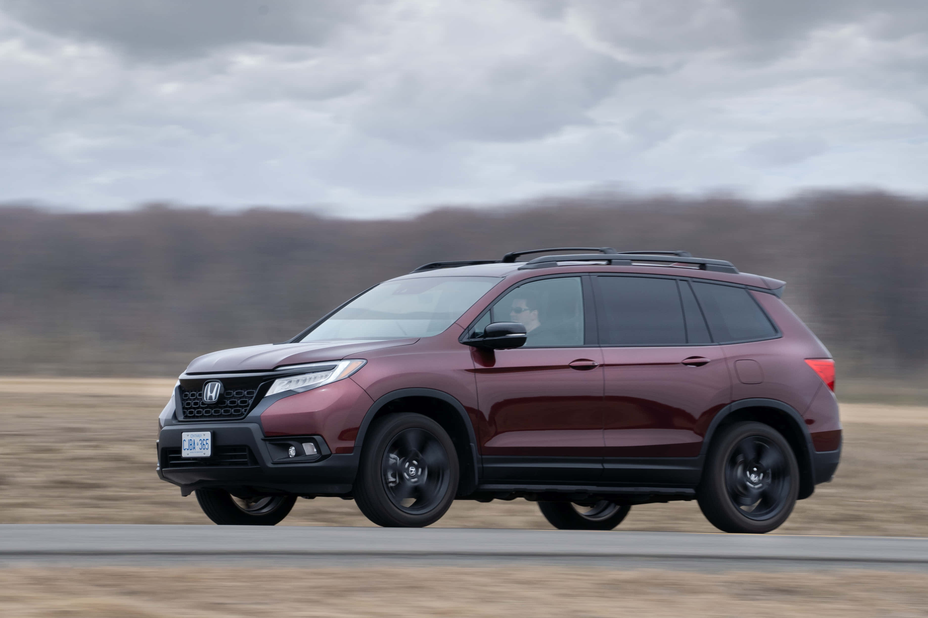Honda Passport 桌布 壁紙 — 一輛栗色本田Pilot SUV在陰天下行駛在鄉村道路上，背景樹木模糊。