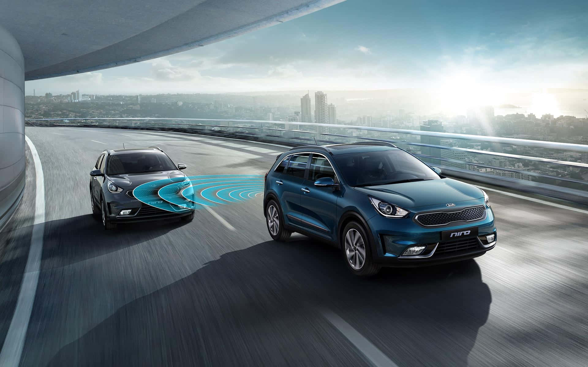 Kia Niro 桌布 壁紙 — 兩部Kia Niro SUV並排行駛在現代化的高架公路上，背景是城市天際線。