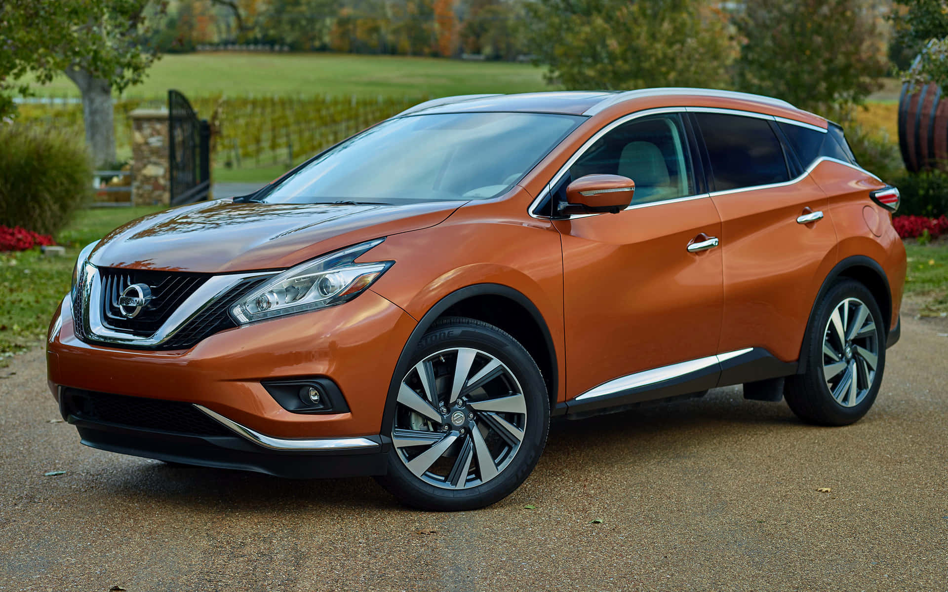 Nissan Murano 桌布 壁紙 — 一架亮橙色日產Murano SUV停泊在碎石車道上，背景有秋天的樹木和石籬笆。