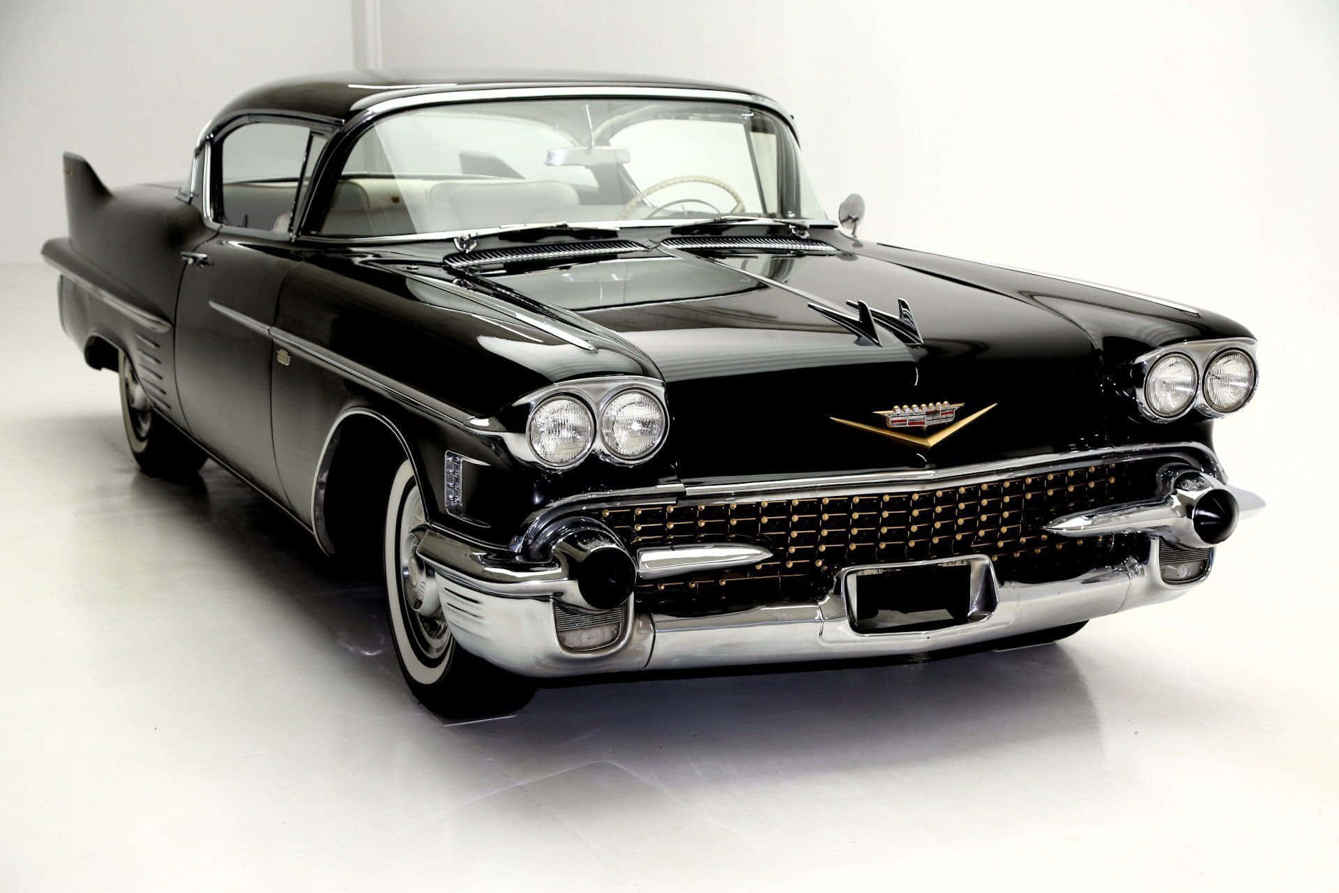 Cadillac Deville 桌布 壁紙 — 一輛光澤黑色1959年凱迪拉克，帶有鍍鉻裝飾和尾鰭，在白色地板上的攝影棚燈光下閃閃發光。