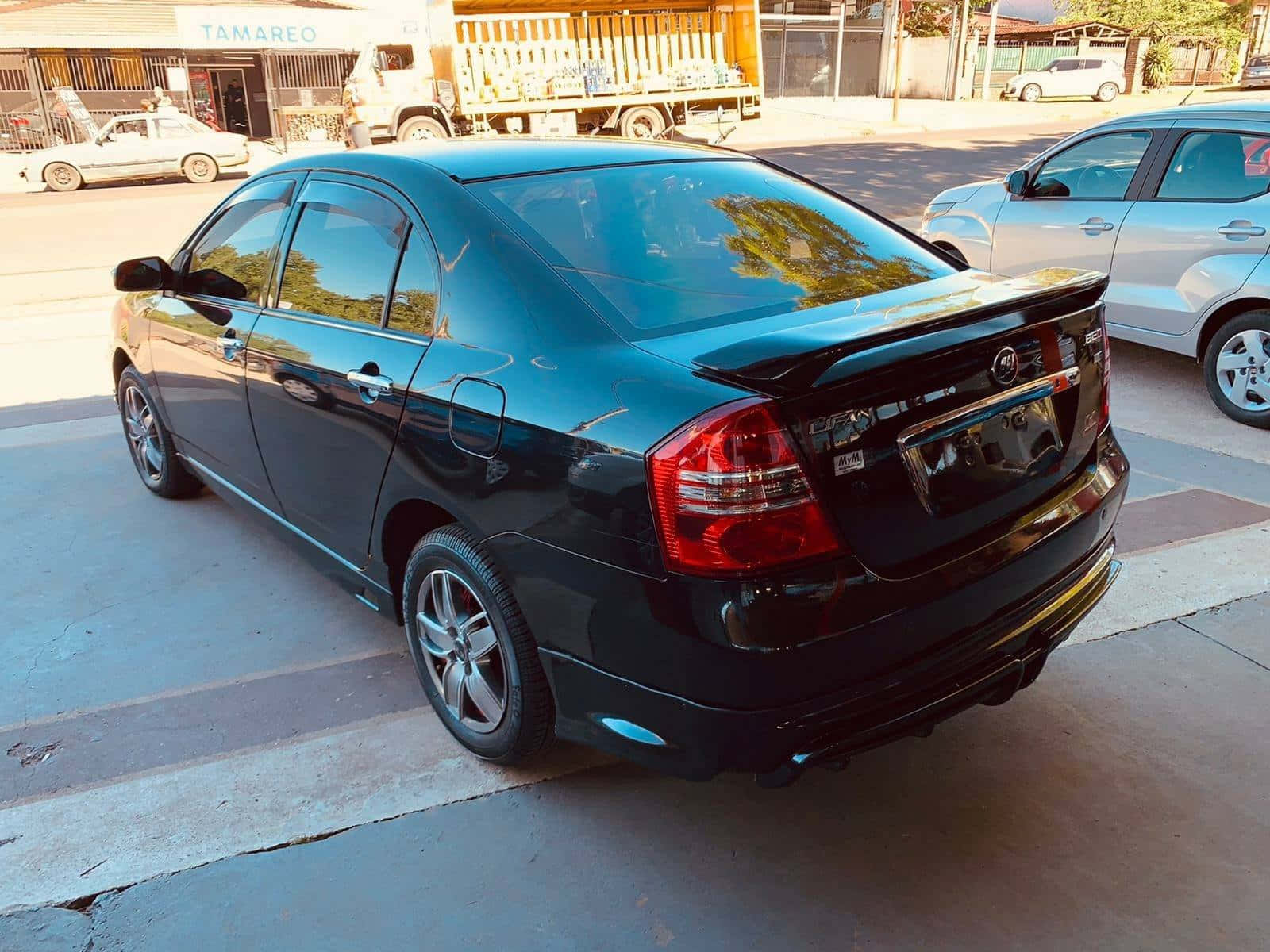  壁紙 — 一架亮黑色轎車停泊在陽光明媚的城市街道上，背景有其他車輛和商店門面。
