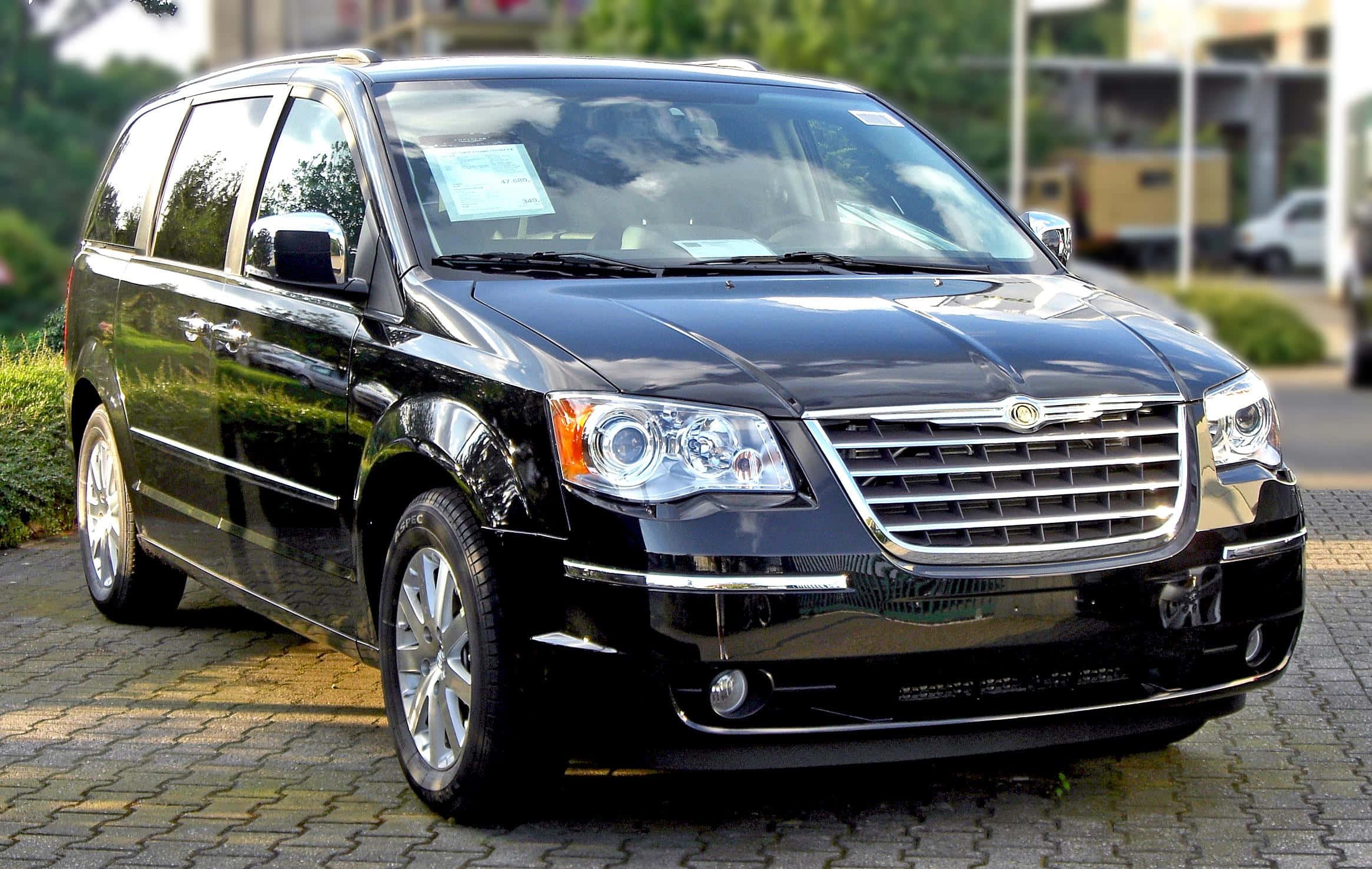 Chrysler Voyager 桌布 壁紙 — 一架亮黑色克萊斯勒 Town & Country 小型貨車停泊在鋪磚的停車場上，背景有綠化和建築物。