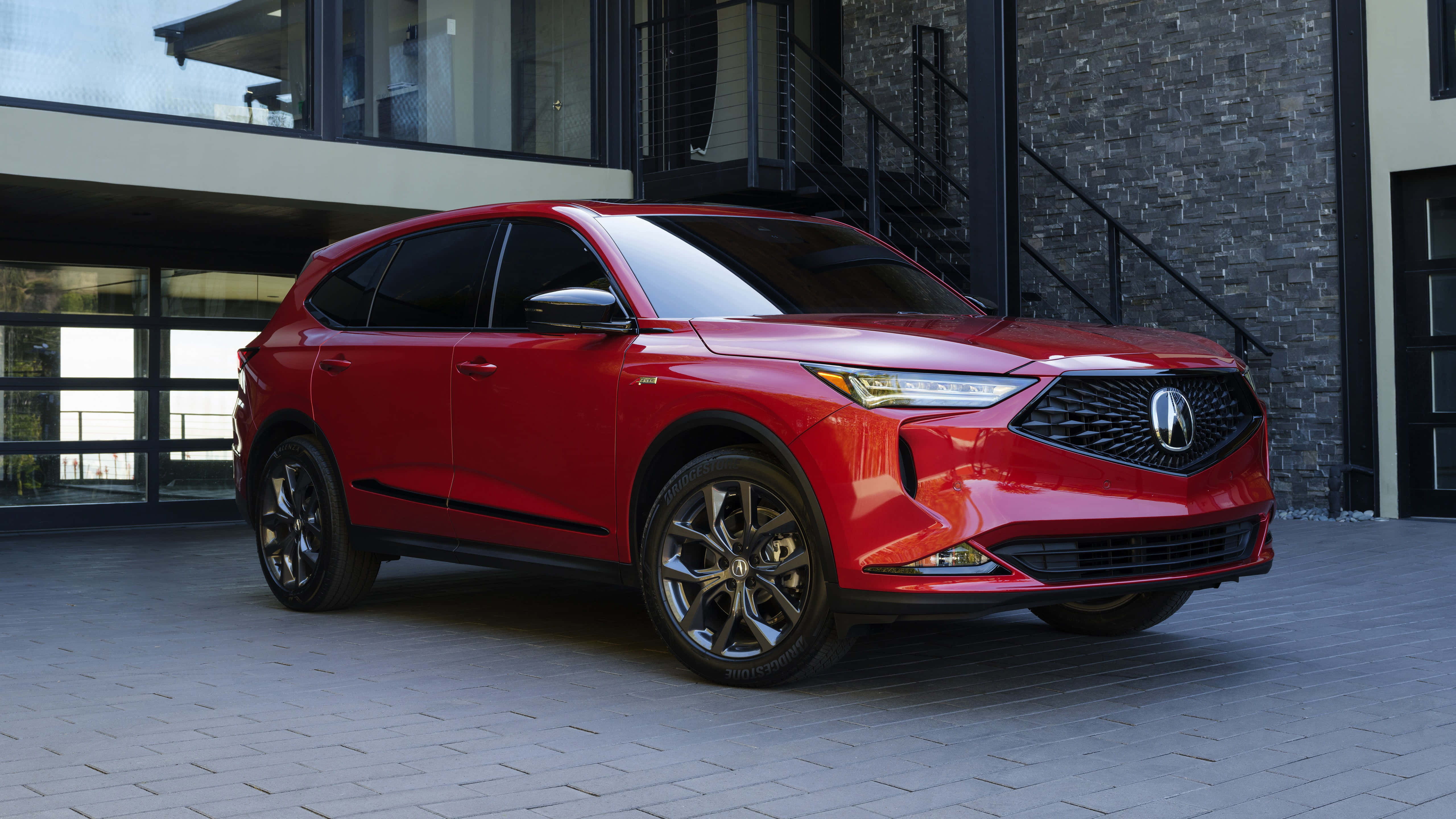 Acura Mdx 桌布 壁紙 — 一輛亮紅色Acura SUV停泊在現代石頭和玻璃建築前的鋪砌庭院。