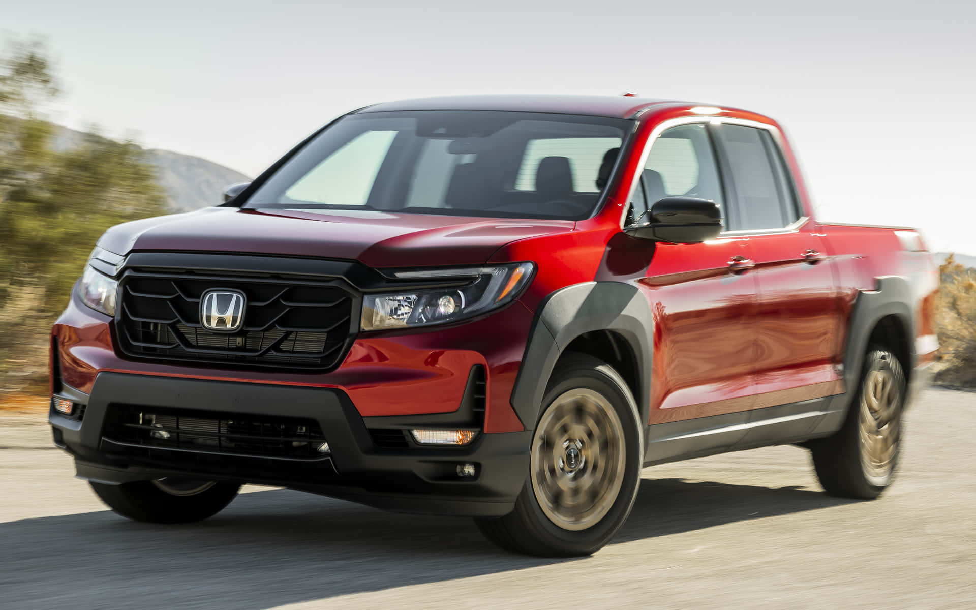 Honda Ridgeline 桌布 壁紙 — 一輛亮紅色的本田Ridgeline皮卡車在沙漠公路上疾馳，帶有模糊的動態效果和遠處的山脈，在明亮的日光下。