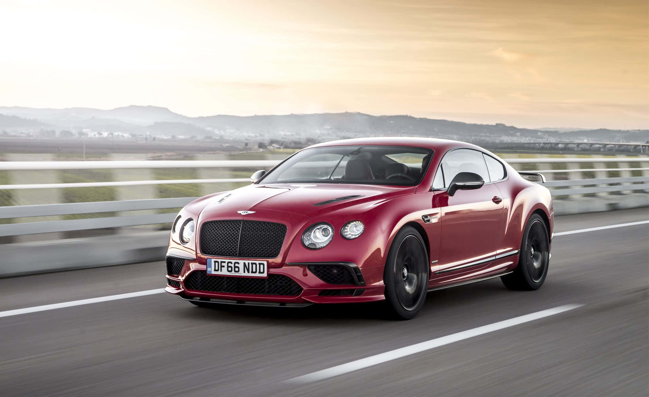 Bentley Continental Supersports 桌布 壁紙 — 一輛亮紅色的賓利Continental GT在黃金時段沿著高速公路橋樑疾馳，帶有模糊的動感和遠處的山丘。