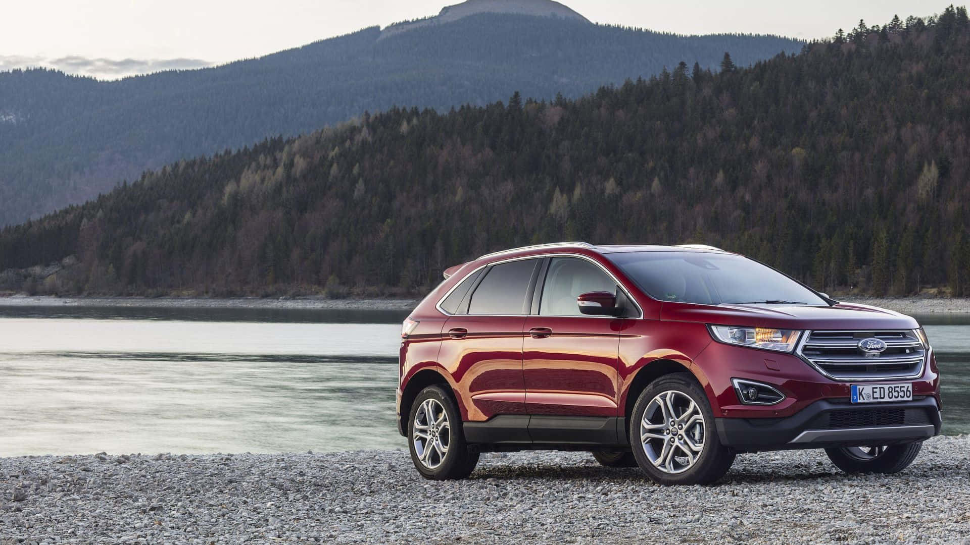 Ford Edge 桌布 壁紙 — 一輛亮紅色的福特Edge SUV停泊在碎石岸邊，旁邊是平靜的水面，背景是森林覆蓋的山脈。