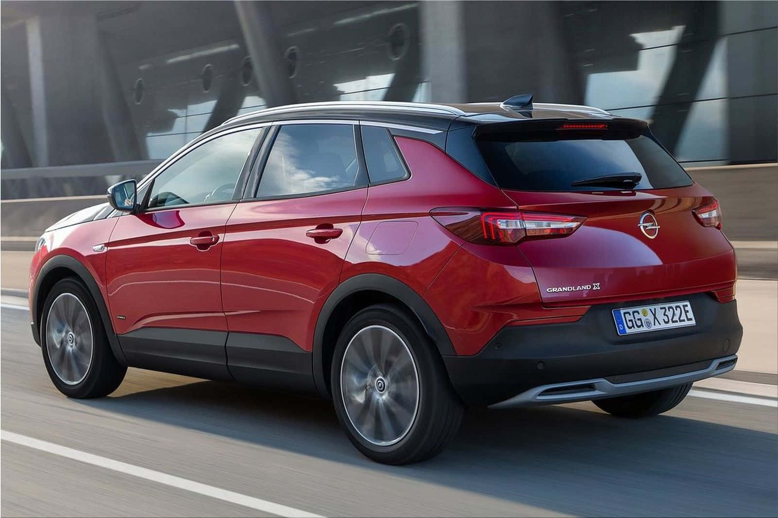 Opel Grandland X 桌布 壁紙 — 一輛亮紅色的Opel Grandland X SUV在現代橋樑上行駛，帶有動態模糊效果，傳達速度與流線設計。
