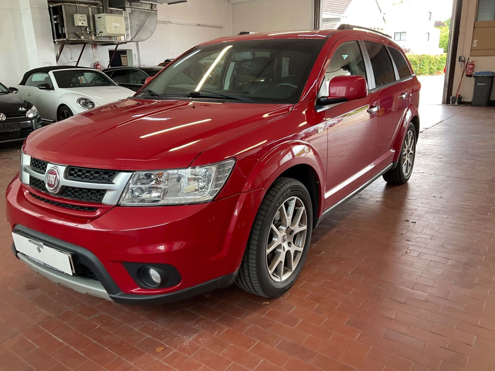  壁紙 — 一輛亮紅色的Dodge Journey SUV停放在光線充足的車庫內，紅色磚地板上，背景可見其他車輛。