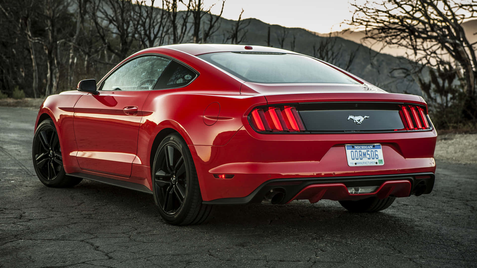 Ford Mustang Ecoboost 桌布 壁紙 — 一輛亮紅色的福特野馬跑車停在日落時分背景有裸樹和山丘的裂縫瀝青路上。