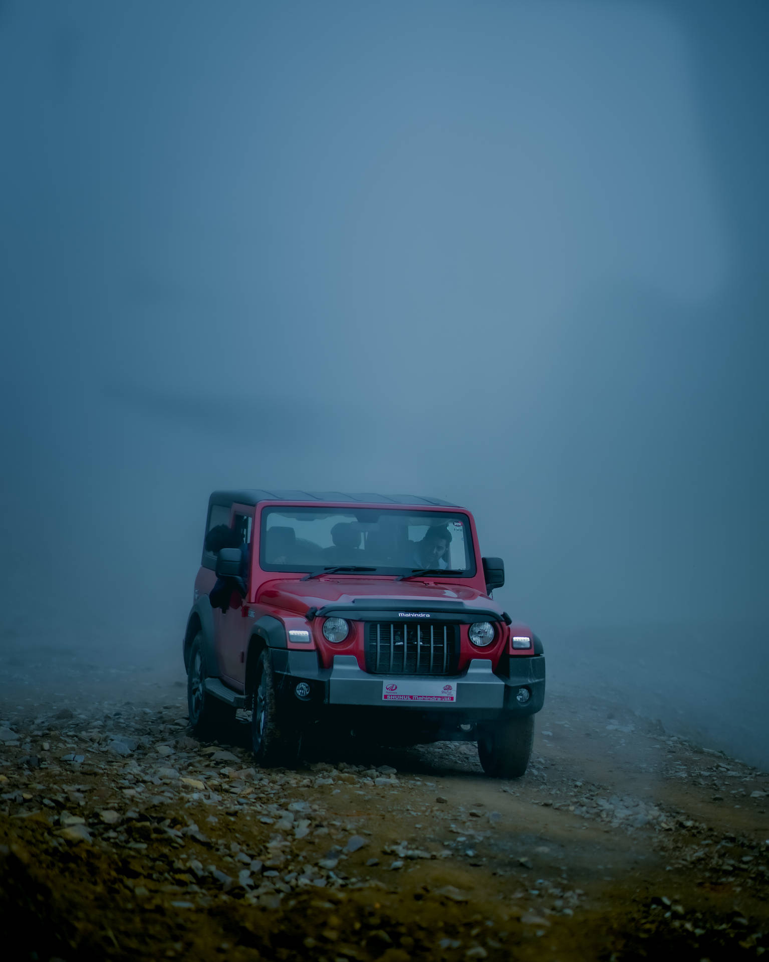 紅色Jeep Wrangler在黃昏時分穿過霧氣瀰漫的山區地形。