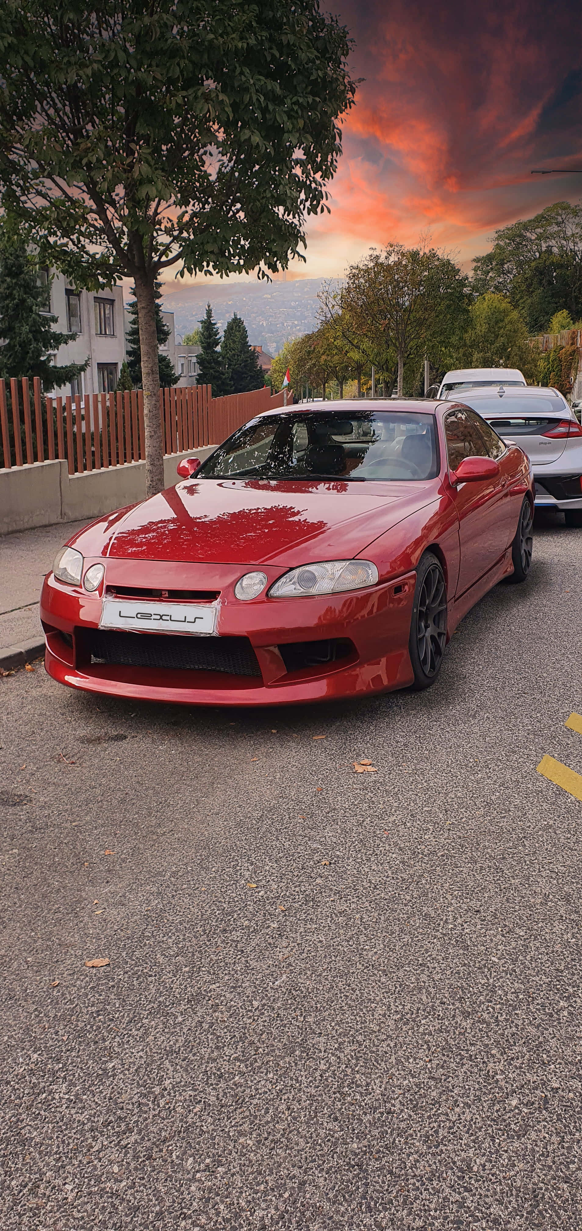 Lexus Sc 300 桌布 壁紙 — 一架亮紅色Lexus跑車停泊在街上，背景是火燒般的夕陽天空，還有樹木和房屋。