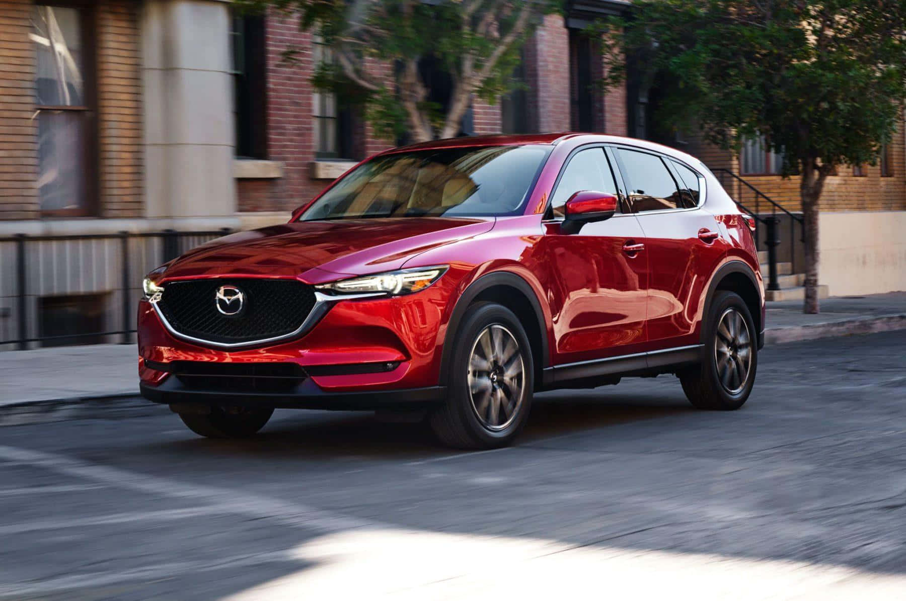 Mazda Cx-5 桌布 壁紙 — 一輛亮紅色的Mazda CX-5 SUV在陽光明媚的城市街道上行駛，磚砌建築和樹木呈現動態模糊效果。