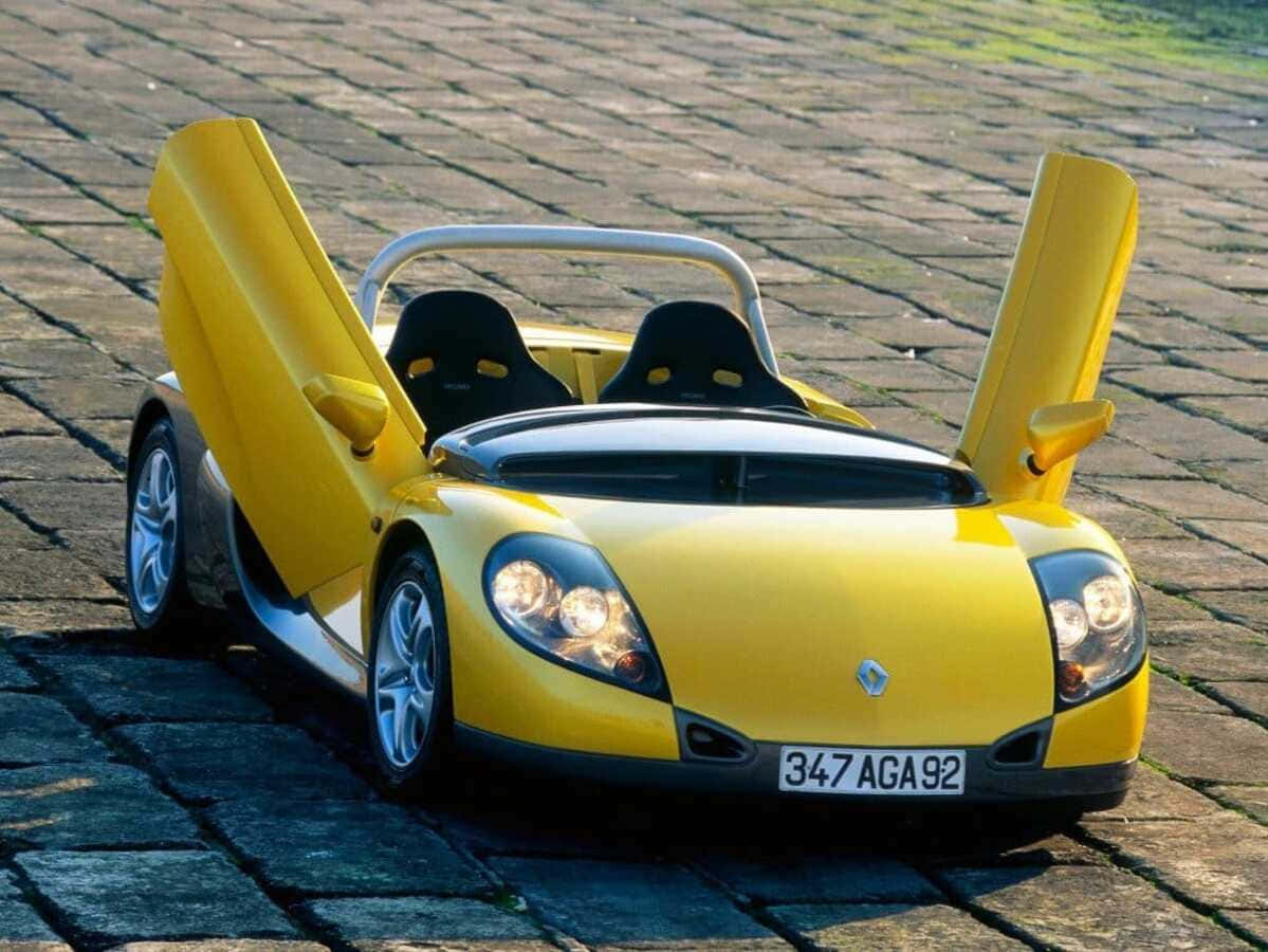 Renault Sport Spider 桌布 壁紙 — 一輛亮黃色的雷諾跑車，鷗翼門打開，停在晴朗日光下的鵝卵石街道上。