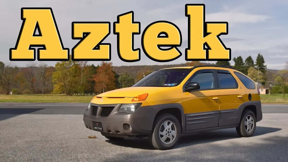  壁紙 — 一輛亮黃色的Pontiac Aztek SUV停泊在瀝青路上，背景是秋天的樹木和山丘，天空多雲。