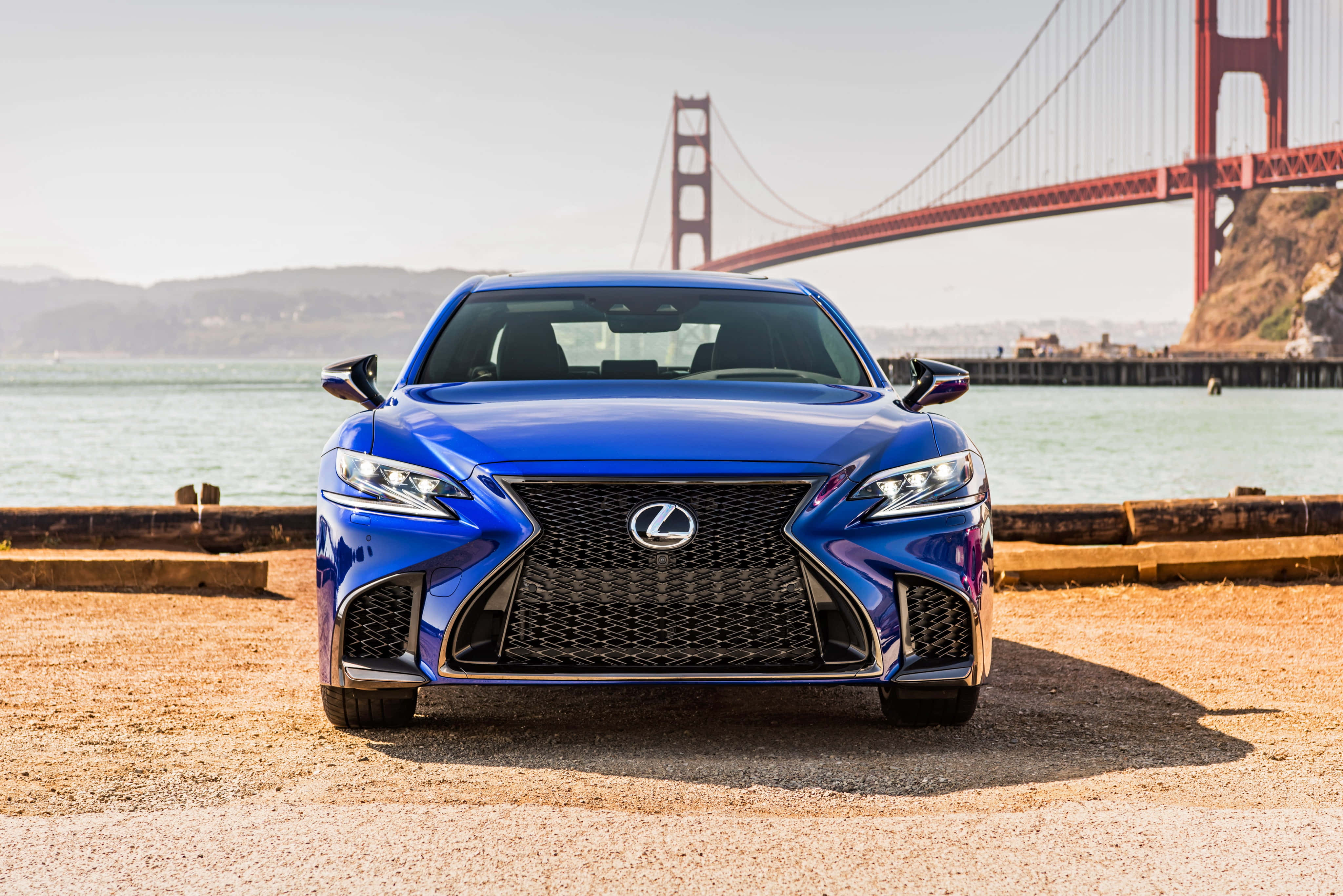 Lexus Ls 500 桌布 壁紙 — 一輛亮藍色Lexus房車面向前方停在碼頭上，背後是晴朗天空下高聳的金門大橋。