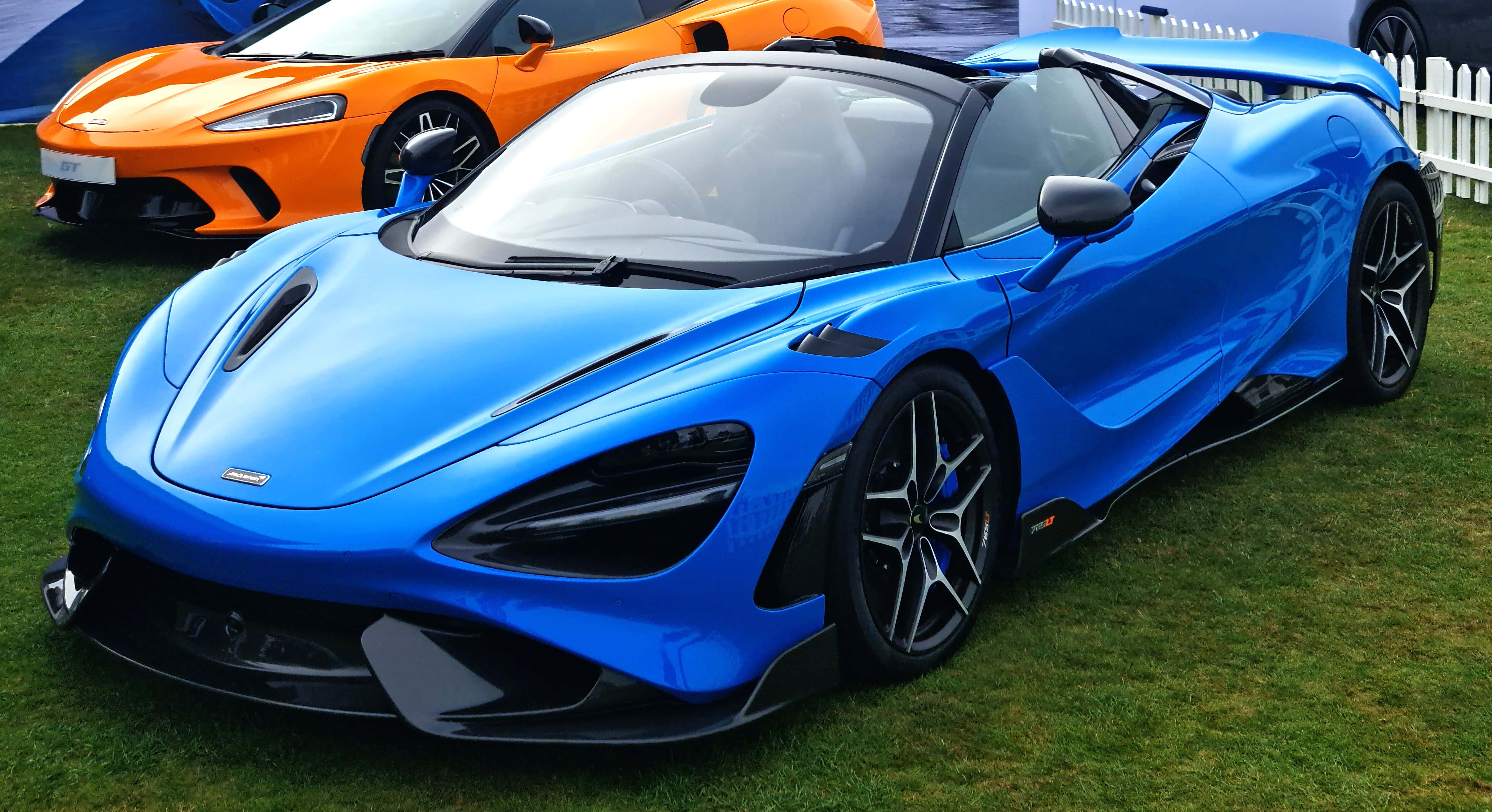 Mclaren 765lt 桌布 壁紙 — 一架亮藍色McLaren Senna跑車停泊在草地上，後面有一輛橙色超級跑車。