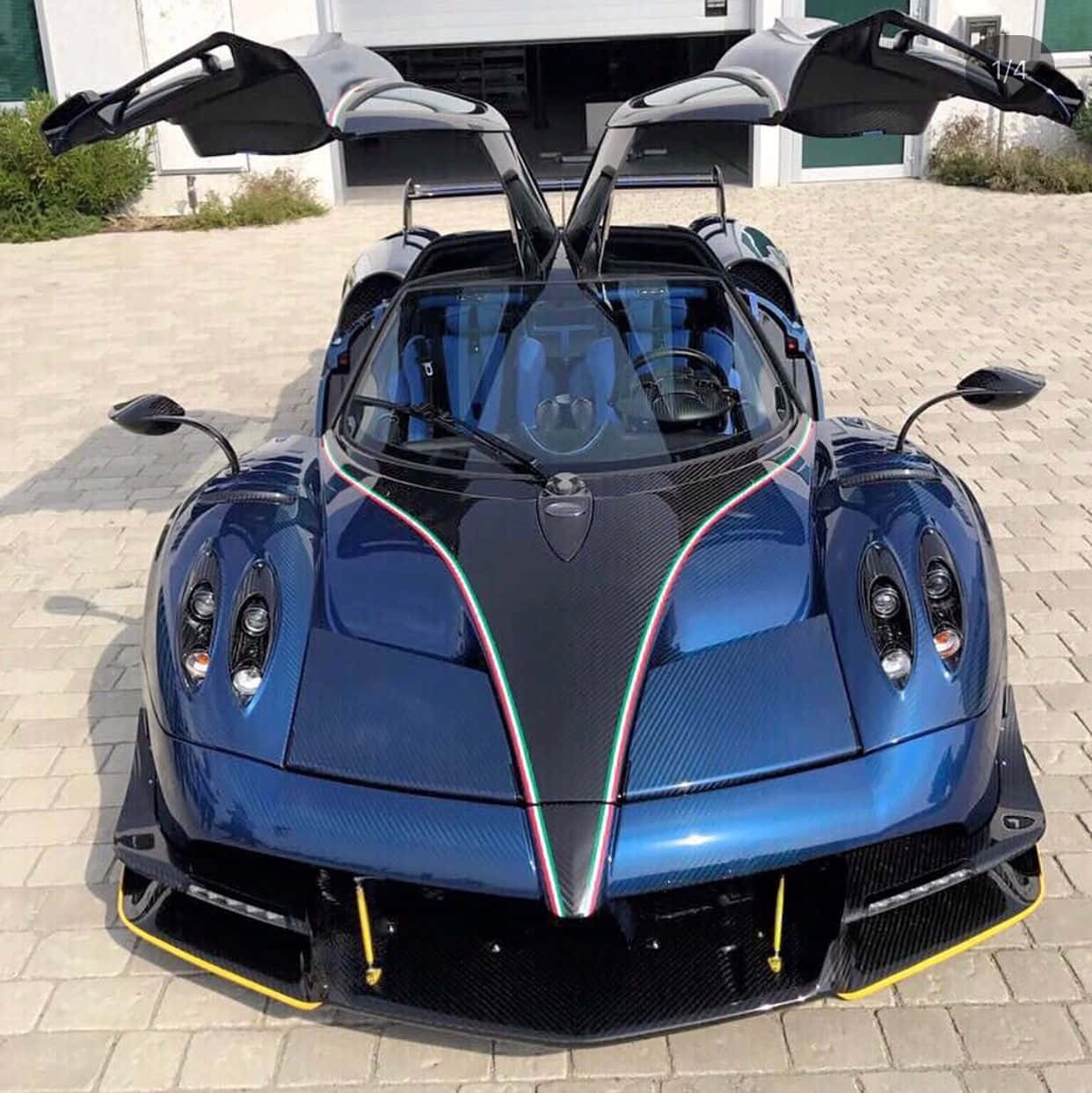 Pagani Zonda Tricolore 桌布 壁紙 — 一輛亮藍色的帕加尼Huayra，剪刀門打開，停在鋪砌的車道上，在明亮的日光下。