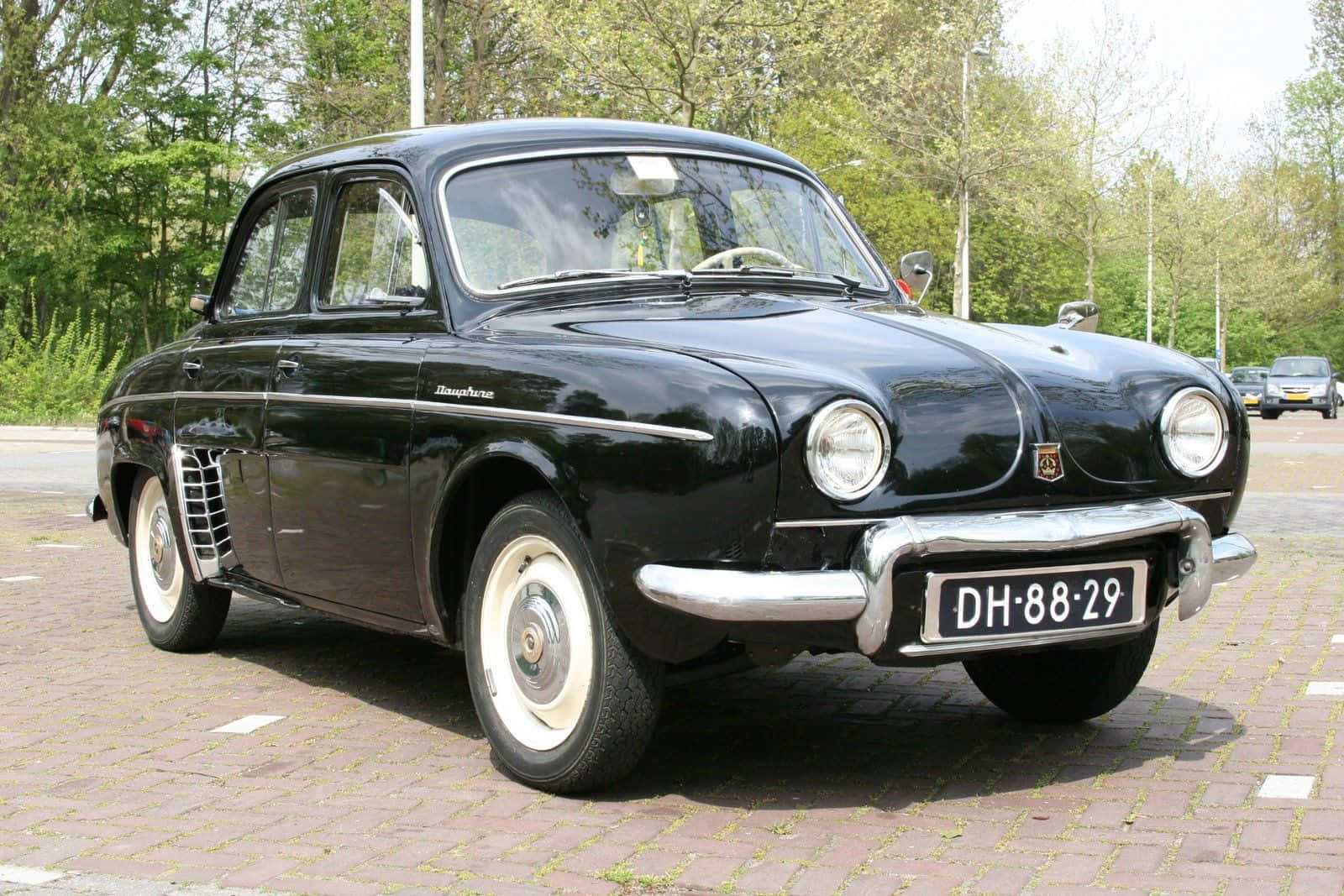 Renault Dauphine 桌布 壁紙 — 一輛亮黑色復古雷諾Dauphine停泊在磚路上，背景有綠色樹木。