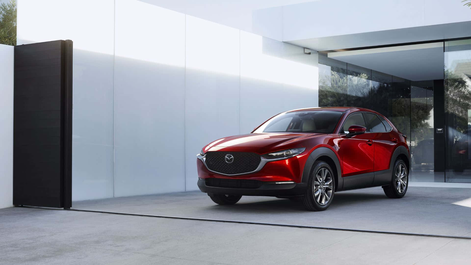 Mazda Cx-3 桌布 壁紙 — 一輛亮紅色的Mazda CX-30 SUV停在一棟現代玻璃與白牆建築前，在明亮的日光下。