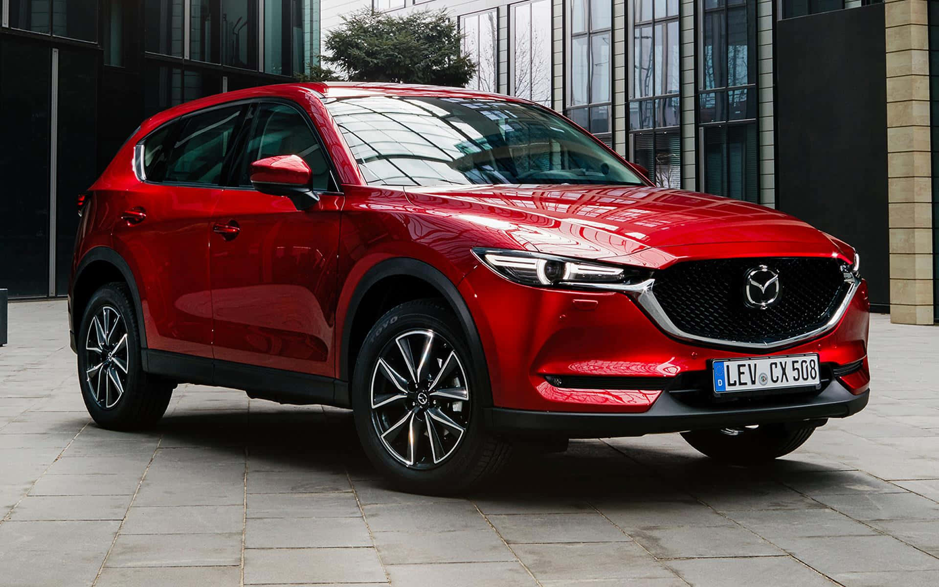 Mazda Cx-5 桌布 壁紙 — 一輛亮紅色Mazda CX-5 SUV停泊在現代玻璃建築前的瓷磚廣場上。
