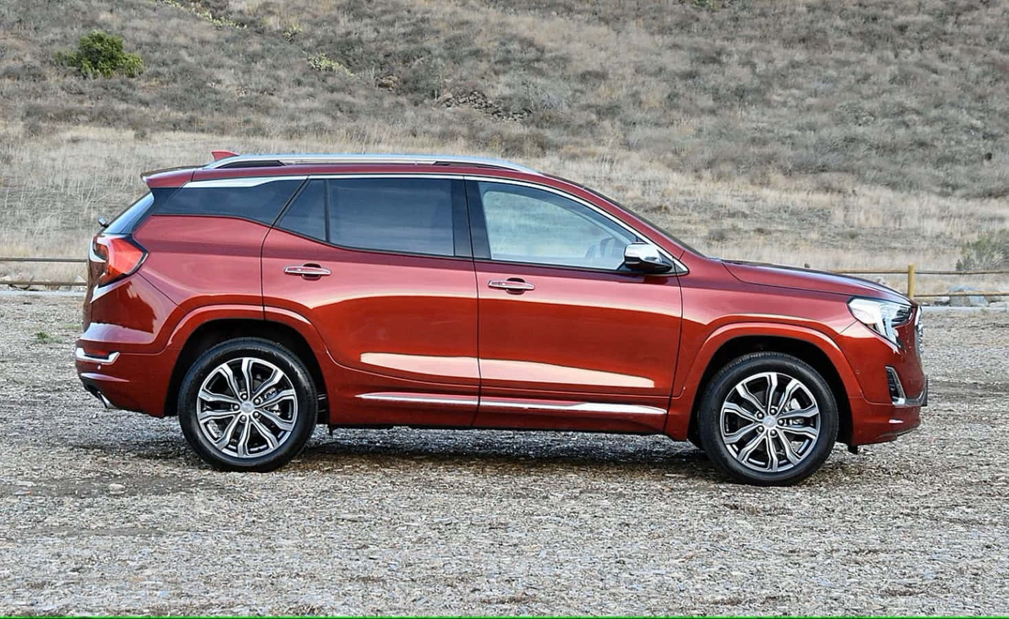 Gmc Terrain 桌布 壁紙 — 一輛亮紅色SUV停泊在碎石上，背景是乾燥的草山，在明亮的日光下。