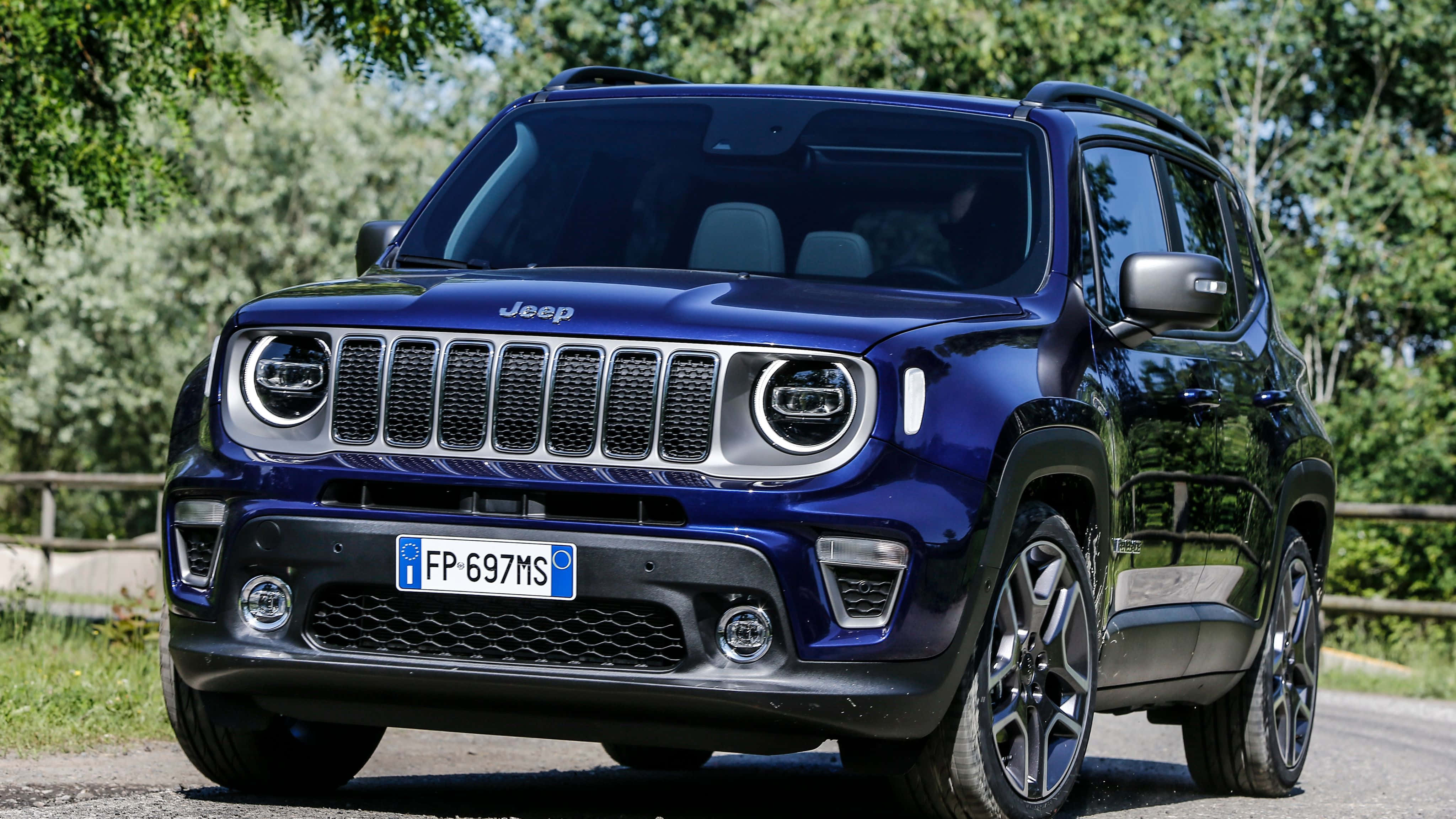 Jeep Renegade 桌布 壁紙 — 一輛亮藍色的Jeep Renegade SUV停在碎石路上，周圍是茂密的綠樹，在明亮的日光下。