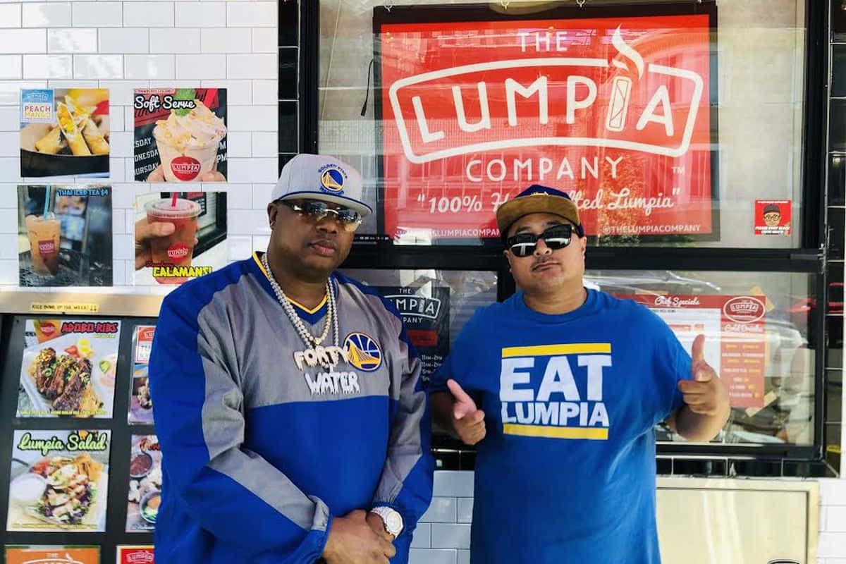  壁紙 — 兩名戴太陽眼鏡和穿隊服的男人自信地在The Lumpia Company美食車外擺姿勢，身後有菜單海報。