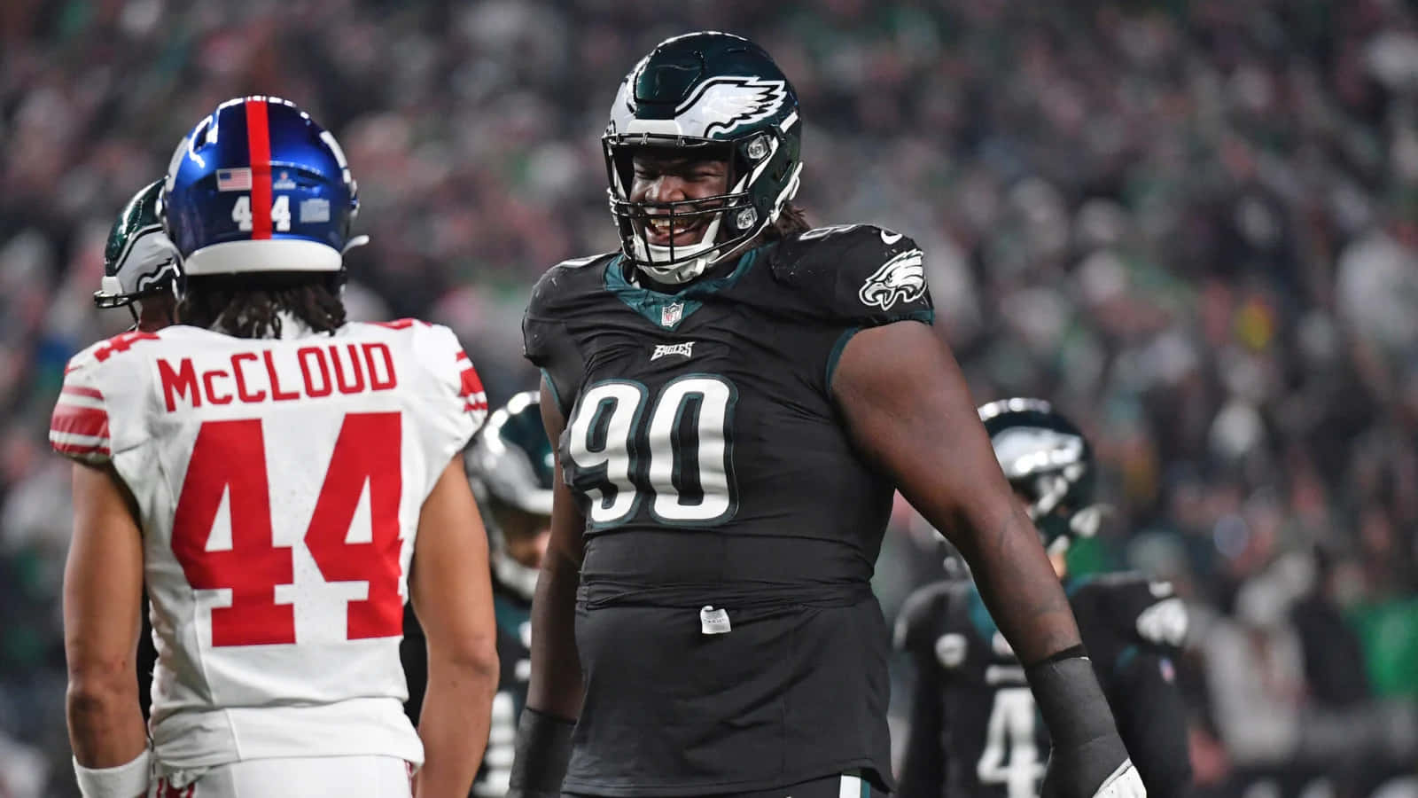  壁紙 — 兩名身穿黑白球衣的NFL球員在擁擠的球場上，在體育場燈光下對峙。