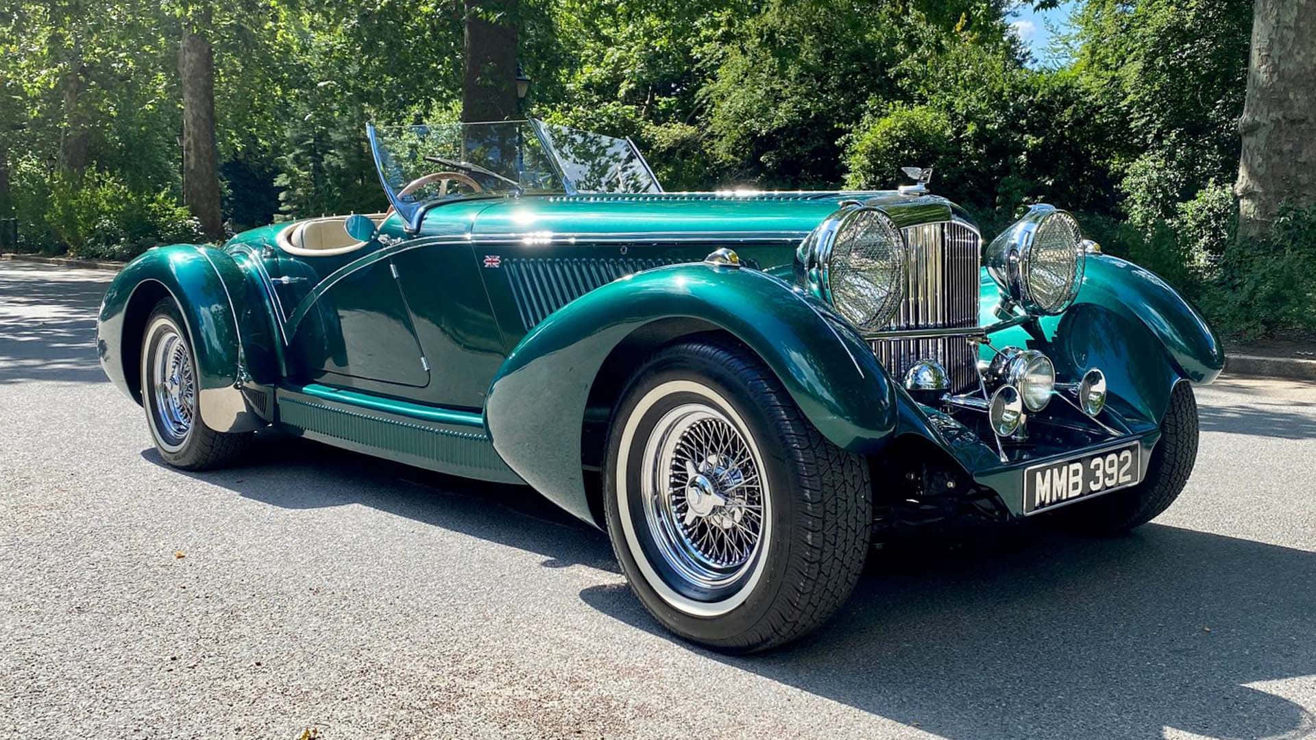 Bentley Mark Vi 桌布 壁紙 — 一輛閃亮的青綠色經典敞篷跑車在明亮的陽光下閃耀，停在綠樹成蔭的瀝青路上。