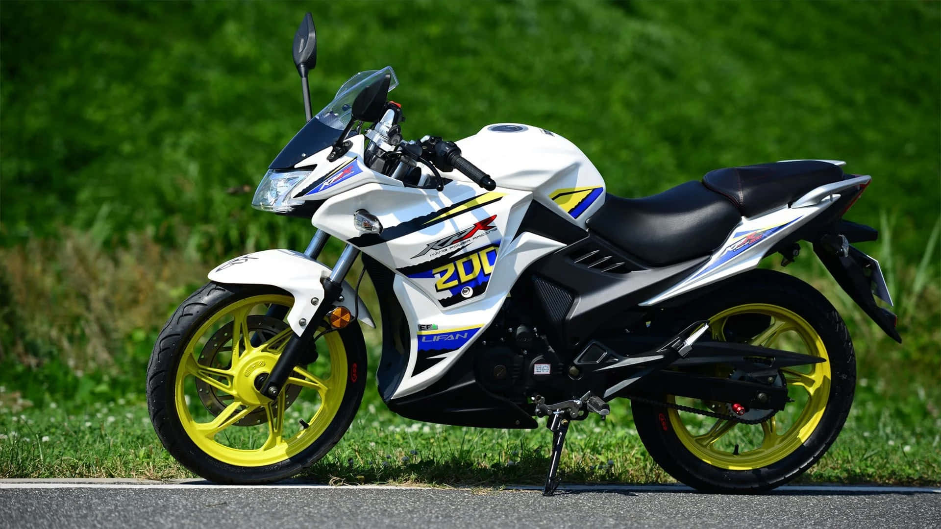 Lifan 200cc 運動摩托車戶外停泊 壁紙 — 一架白色和黃色的運動摩托車，帶有黑色點綴，停在鋪砌的道路上，旁邊是茂密的綠草，在明亮的日光下。