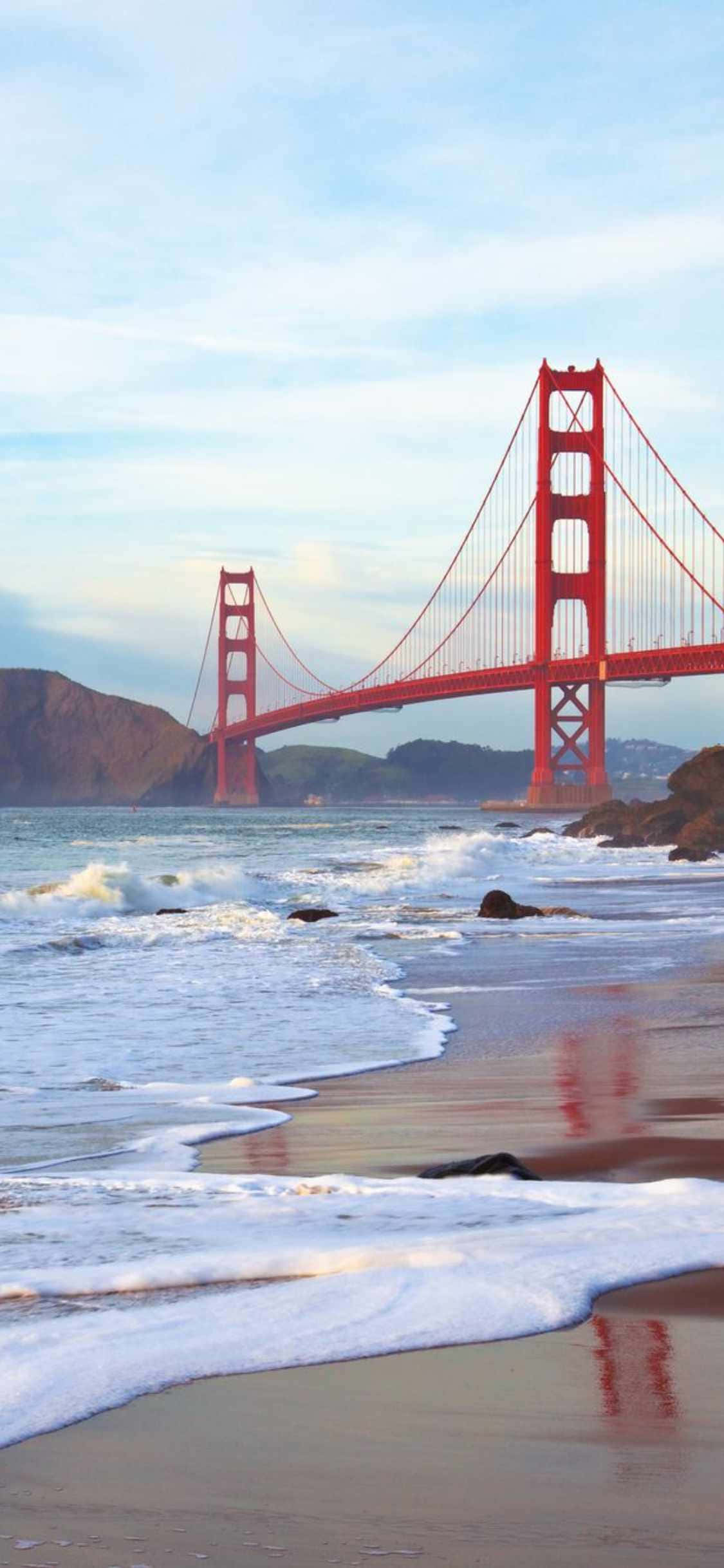 「Life's A Beach with iPhone Xs Malibu」 壁紙 — 標誌性的紅色金門大橋橫跨海灣，海浪拍打，沙灘在柔和的藍天下。