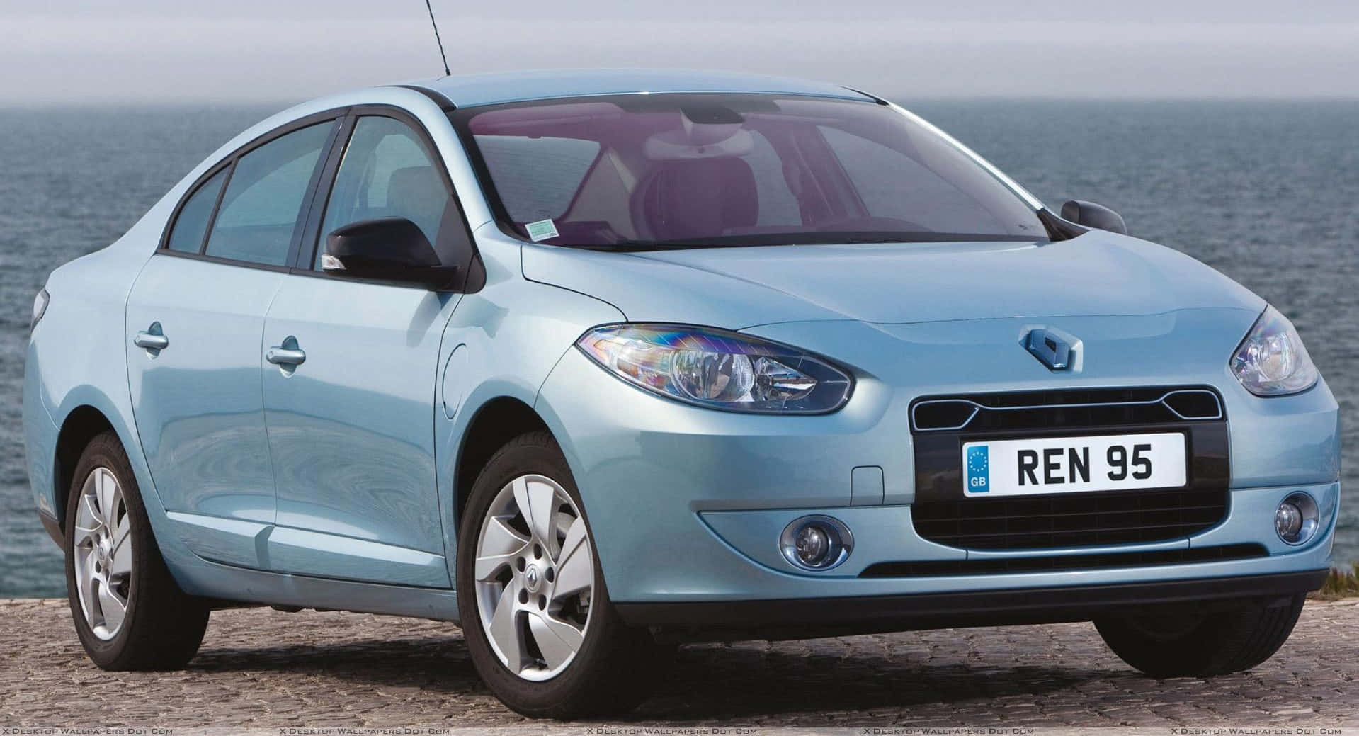 Renault Fluence 桌布 壁紙 — 一輛淺藍色雷諾房車停泊在岩石海岸上，背景是陰天下的海浪。