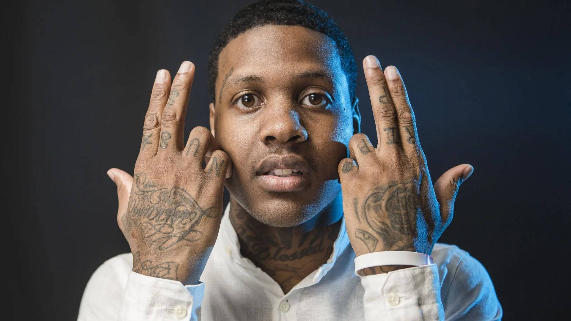 Lil Durk 肖像照 壁紙 — 一名手部和頸部有紋身的男子在深色背景下，在冷藍色燈光下強烈擺姿勢。