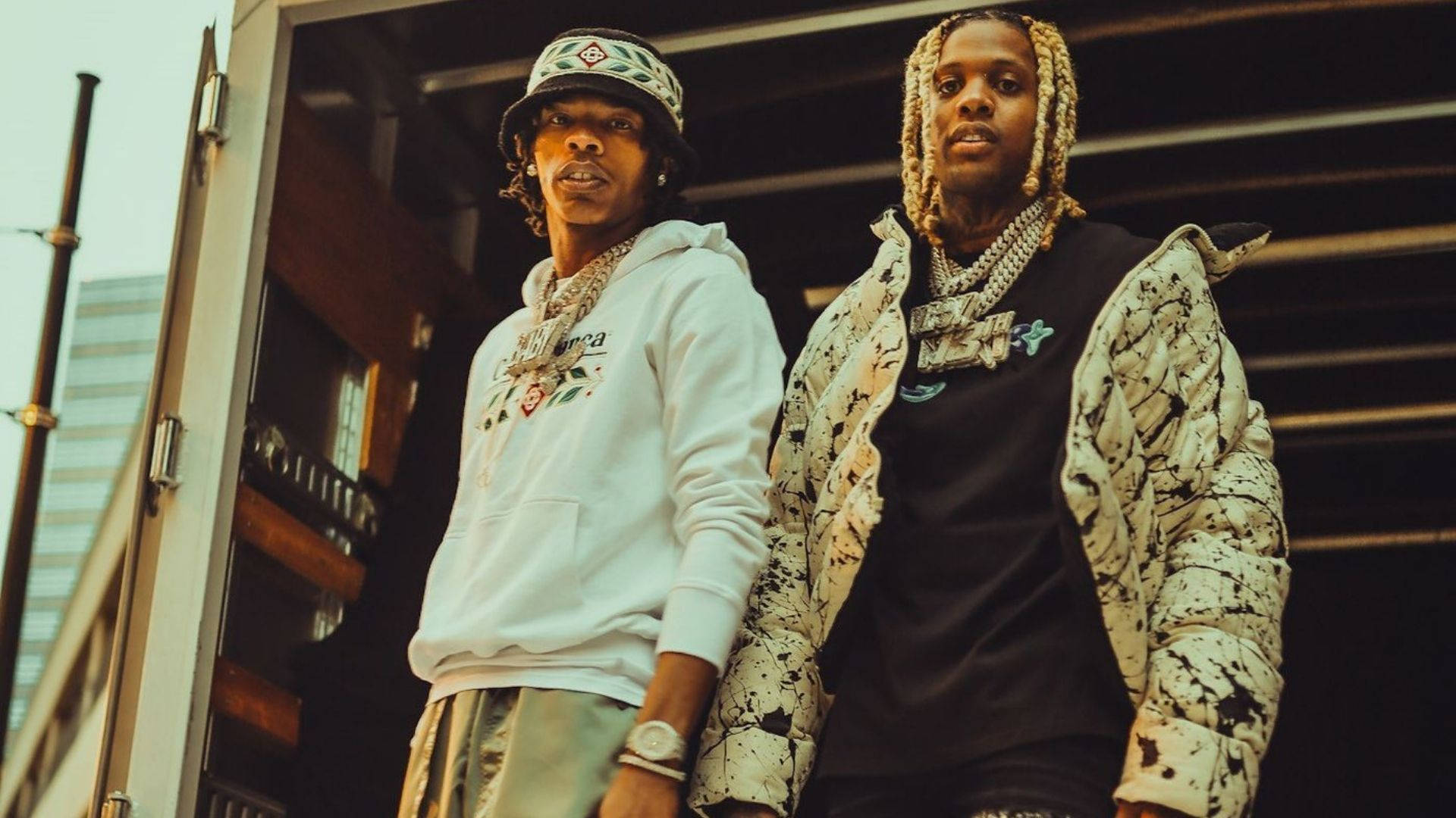 Lil Durk 與 Lil Baby 戶外合影 壁紙 — 兩位時尚的饒舌歌手在粗獷的城市背景下，自信地穿著都市街頭服飾，配以大膽的珠寶和富有表現力的造型。