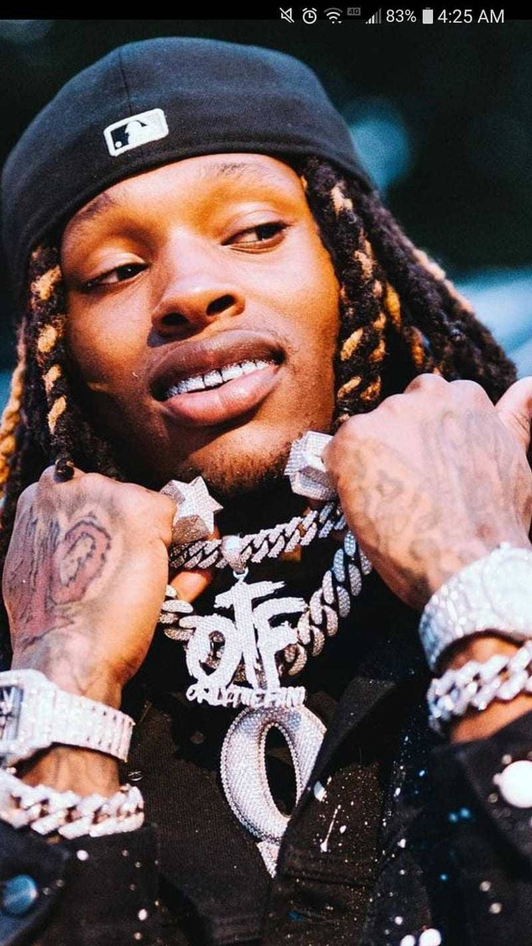 Lil Durk 舞台熱情演出 壁紙 — 一名辮子男子戴黑色帽子及閃亮鑽石首飾，背景模糊的特寫肖像。