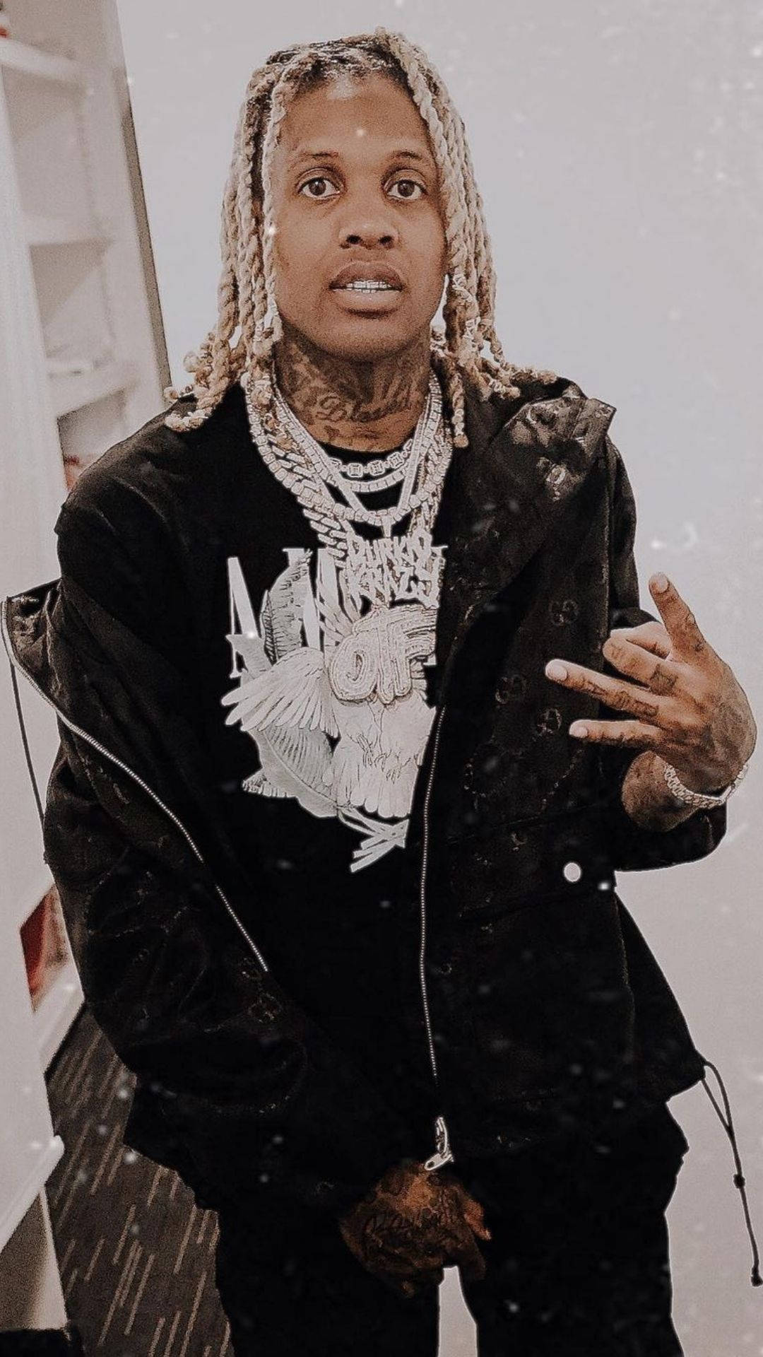 Lil Durk 衣櫥內造型 壁紙 — 一名辮髮紋身男子身穿帶銀鏈的黑色外套，在室內做出手勢。