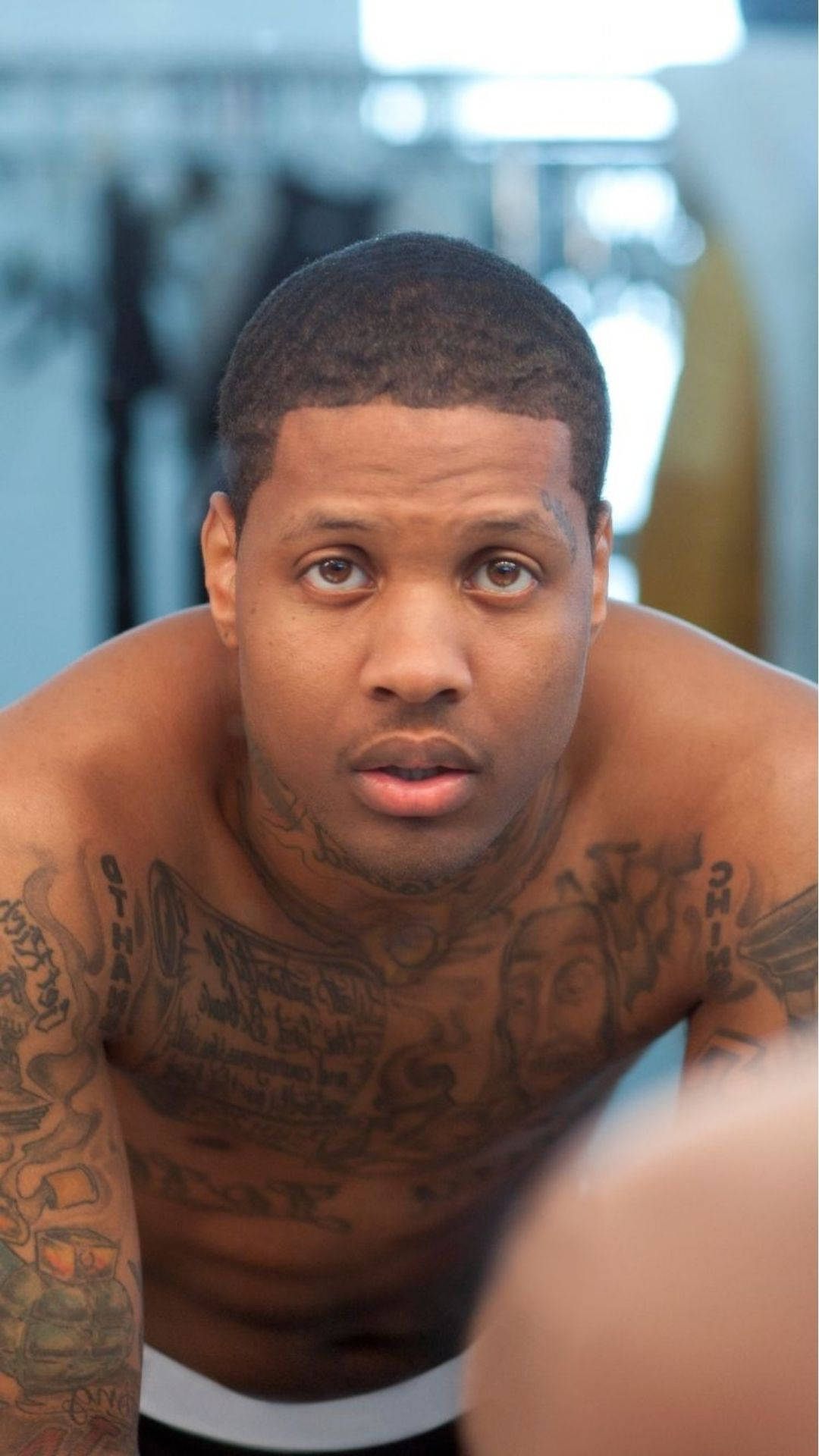 Lil Durk 赤裸上身 壁紙 — 一個冇著衫、全身紋身嘅男人喺燈光充足嘅健身室入面，專注咁望住鏡頭。