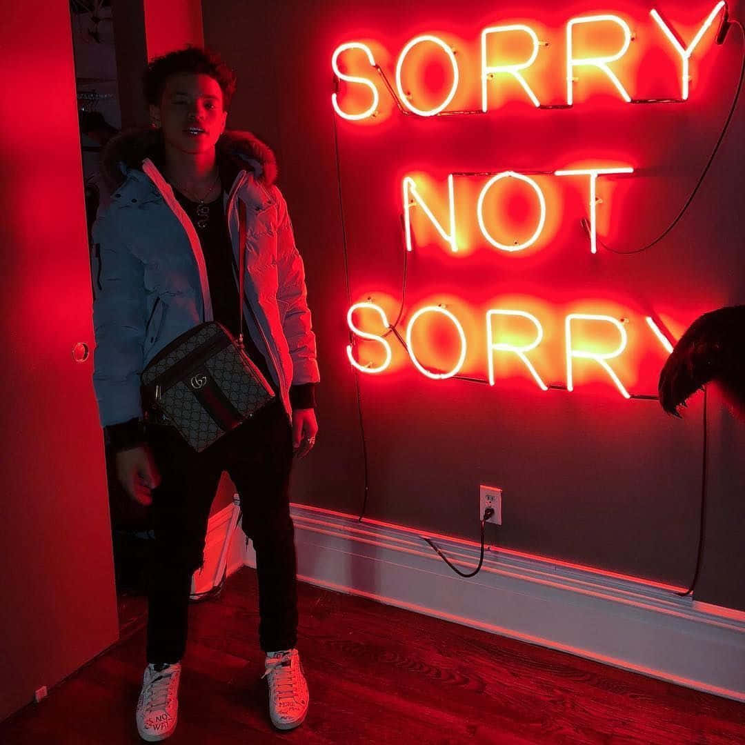 身穿外套和運動鞋的年輕男子站在寫著 sorry not sorry 的紅色霓虹燈標誌前。