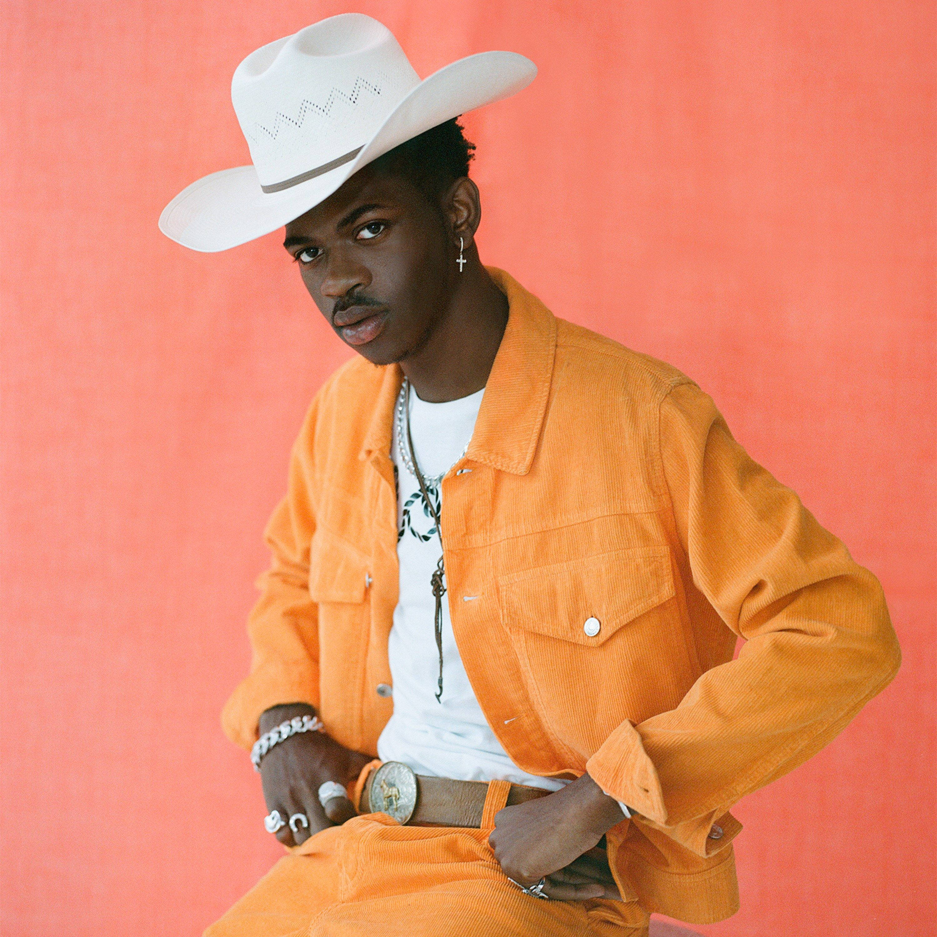 Lil Nas X Teen Vogue 照片拍攝 壁紙 — 一位時尚的年輕男子戴著白色牛仔帽，穿著橙色燈芯絨套裝，在珊瑚粉色的攝影棚背景前自信地擺姿勢。